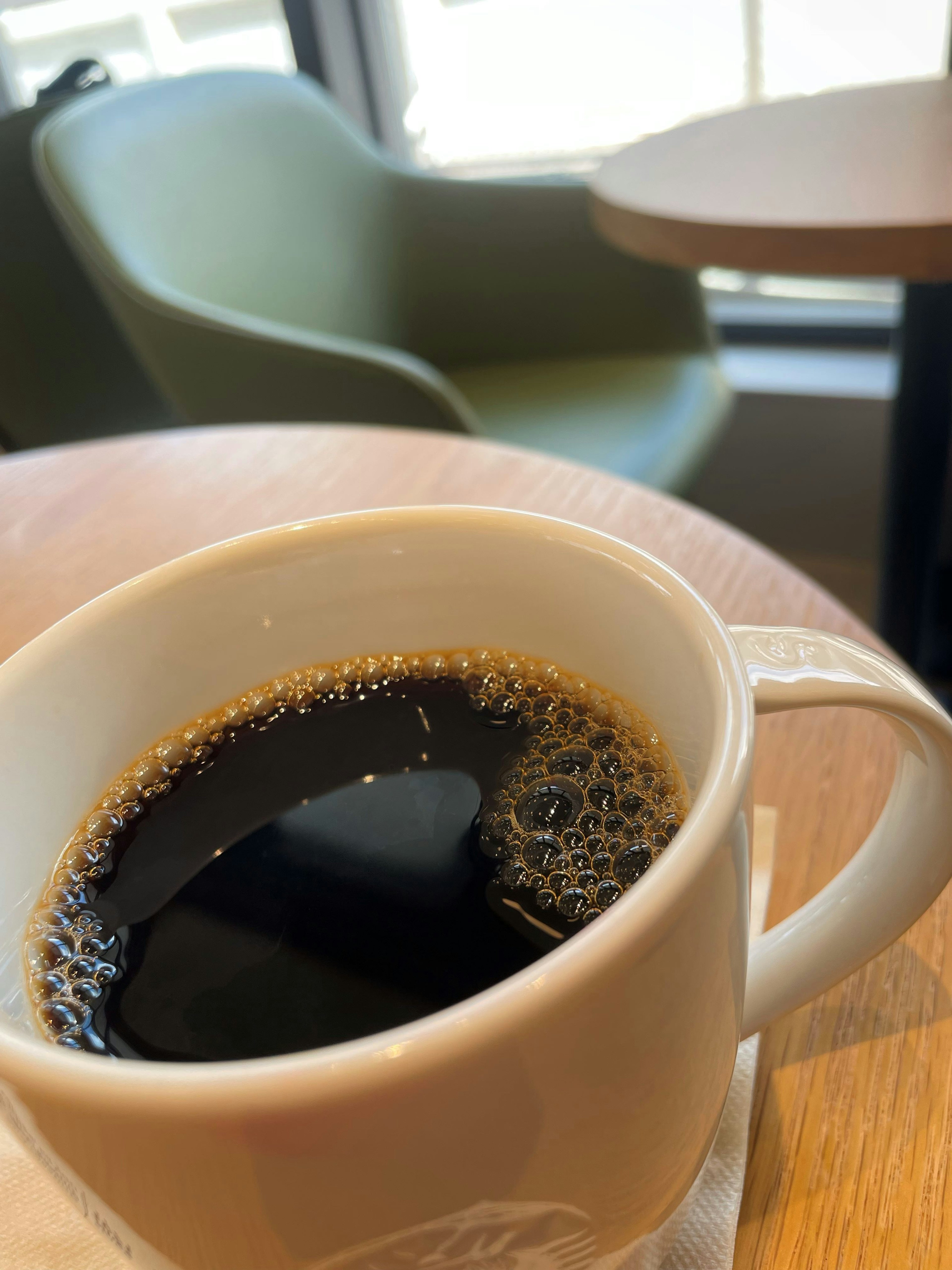 Close-up of a coffee cup with black coffee and a soft green chair in the background