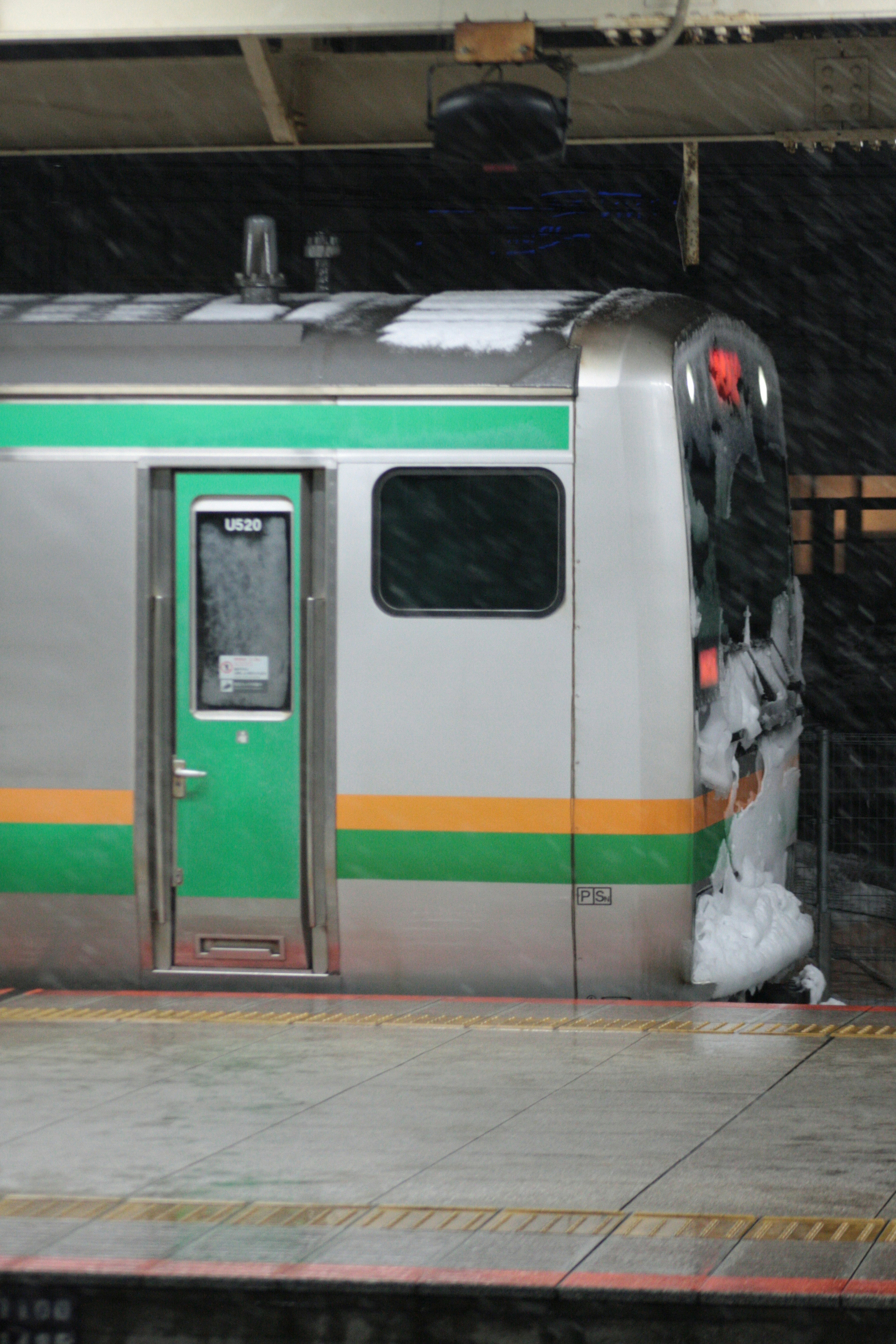 Vista laterale di un treno coperto di neve con strisce verdi e arancioni