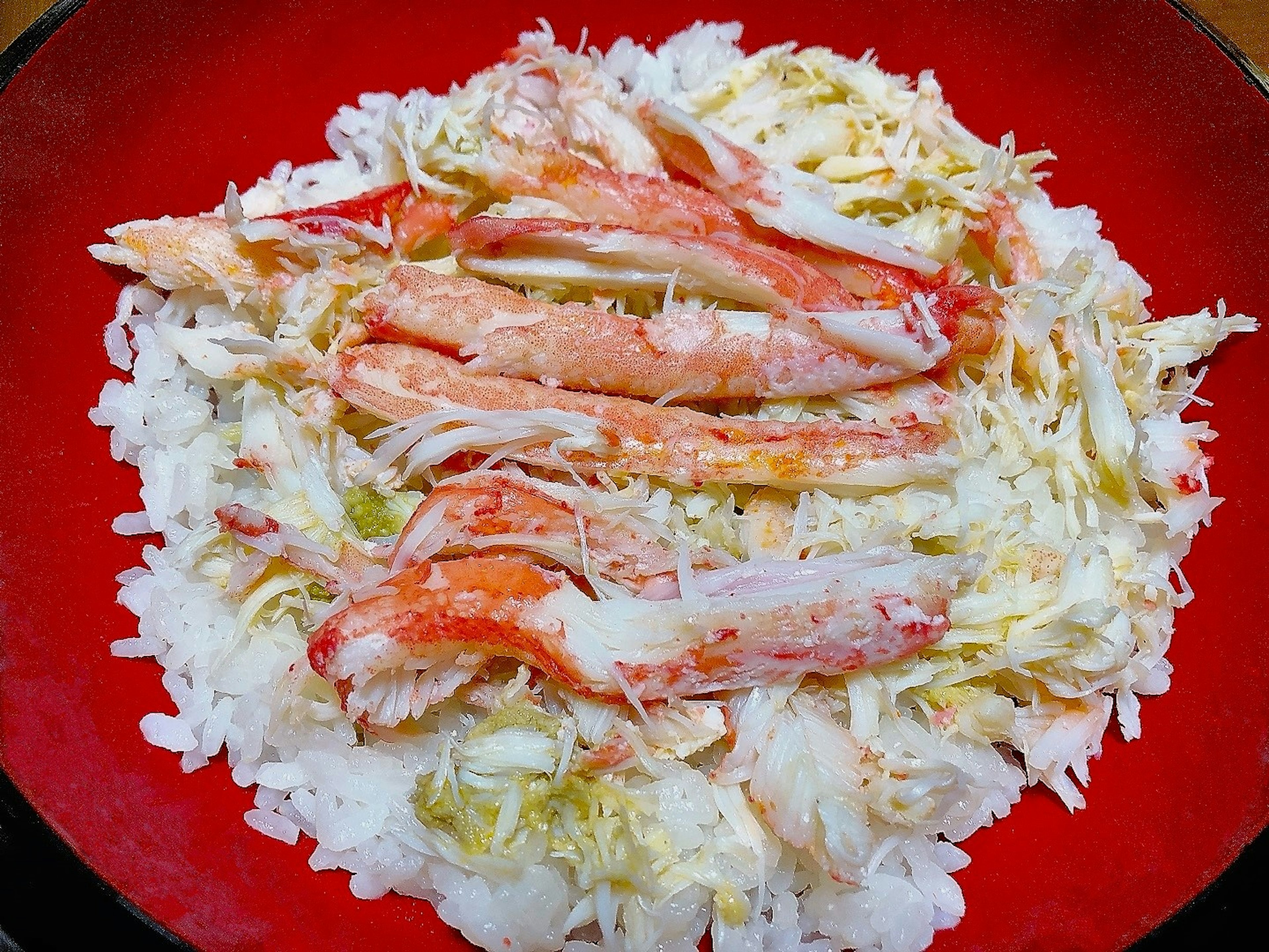 Dish of white rice topped with crab meat and cabbage served on a red plate