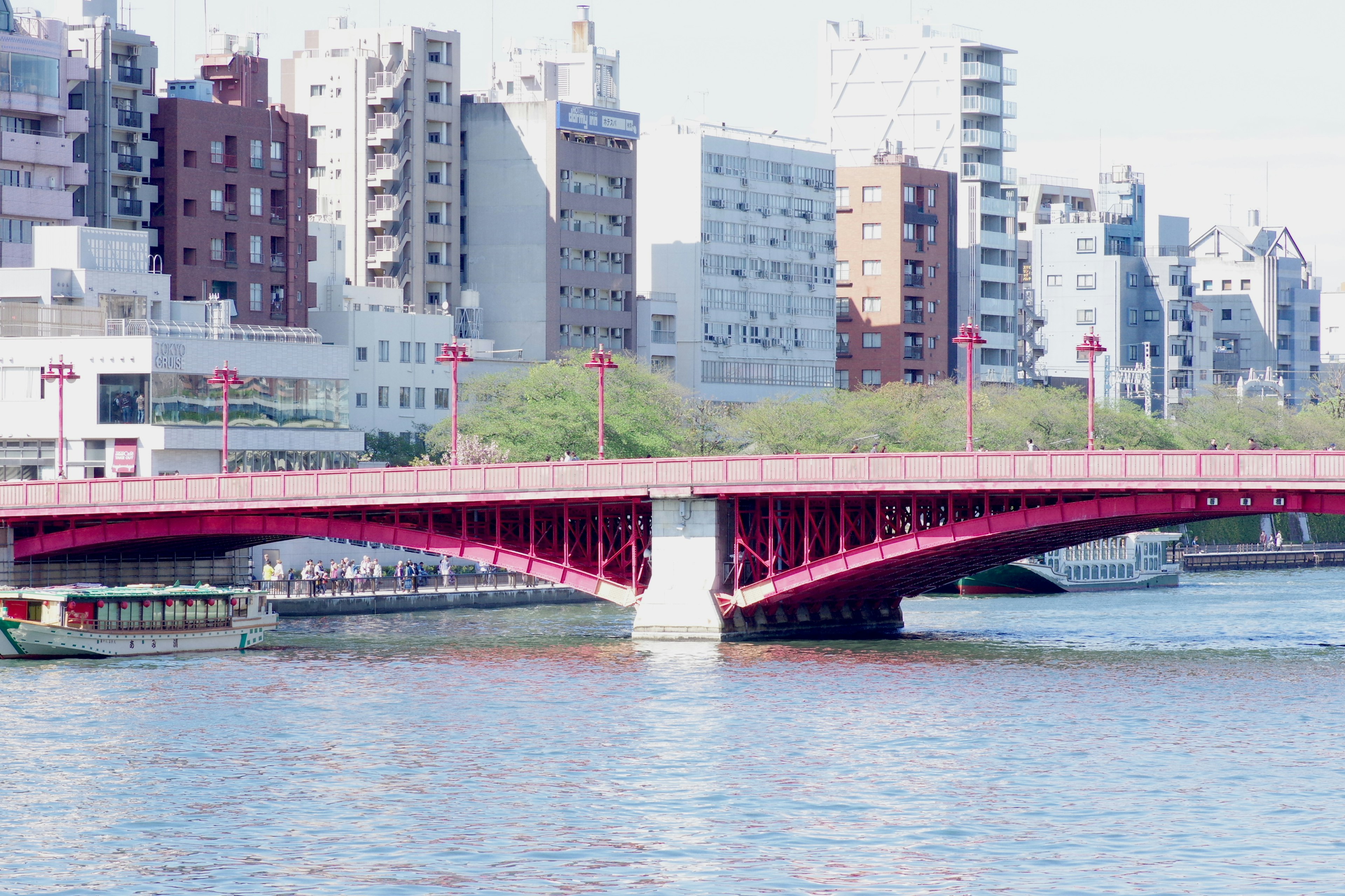 Red bridge spanning a river with urban buildings in the background