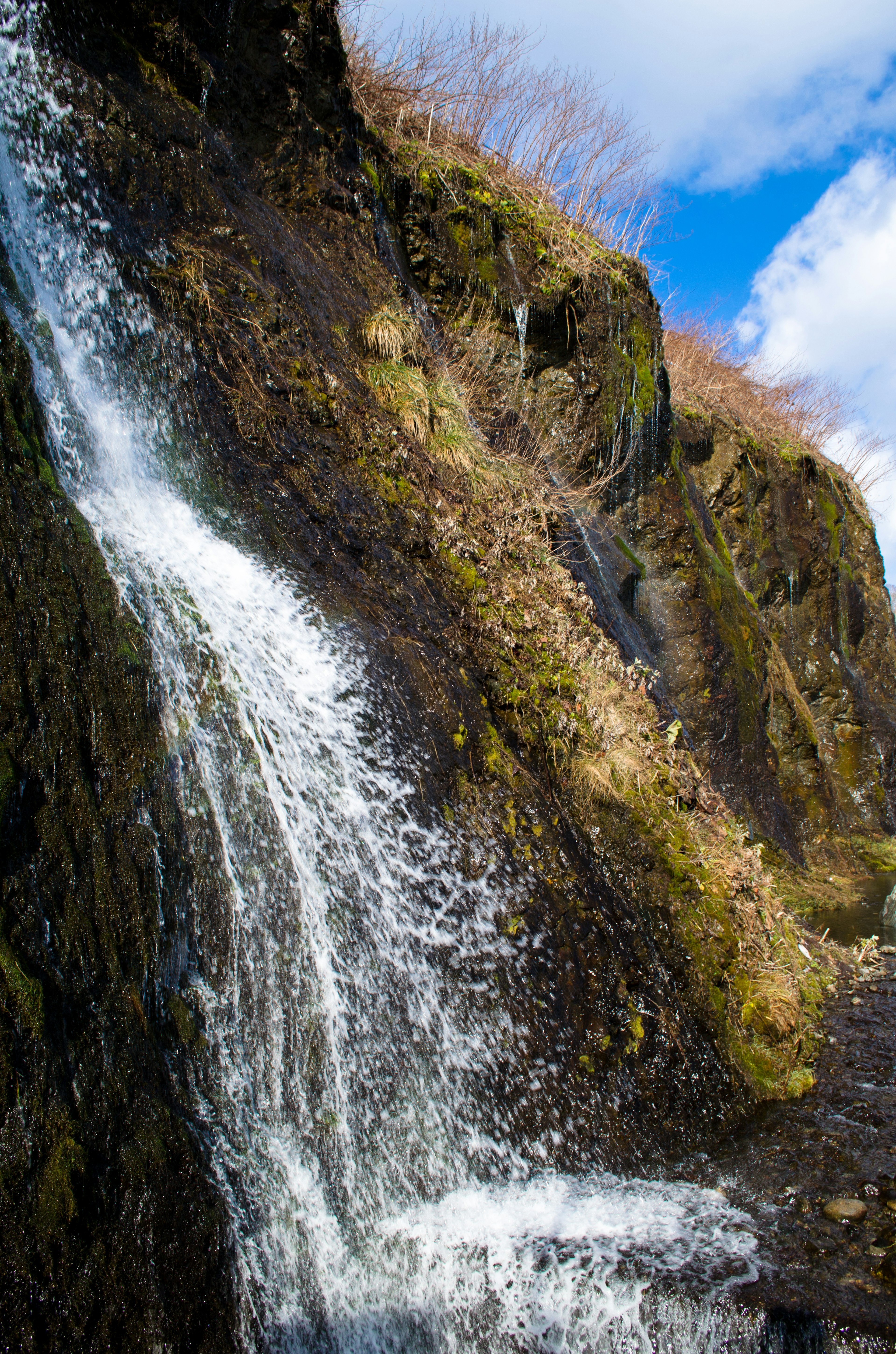 Wasserfall, der über moosbedeckte Felsen unter einem blauen Himmel fließt