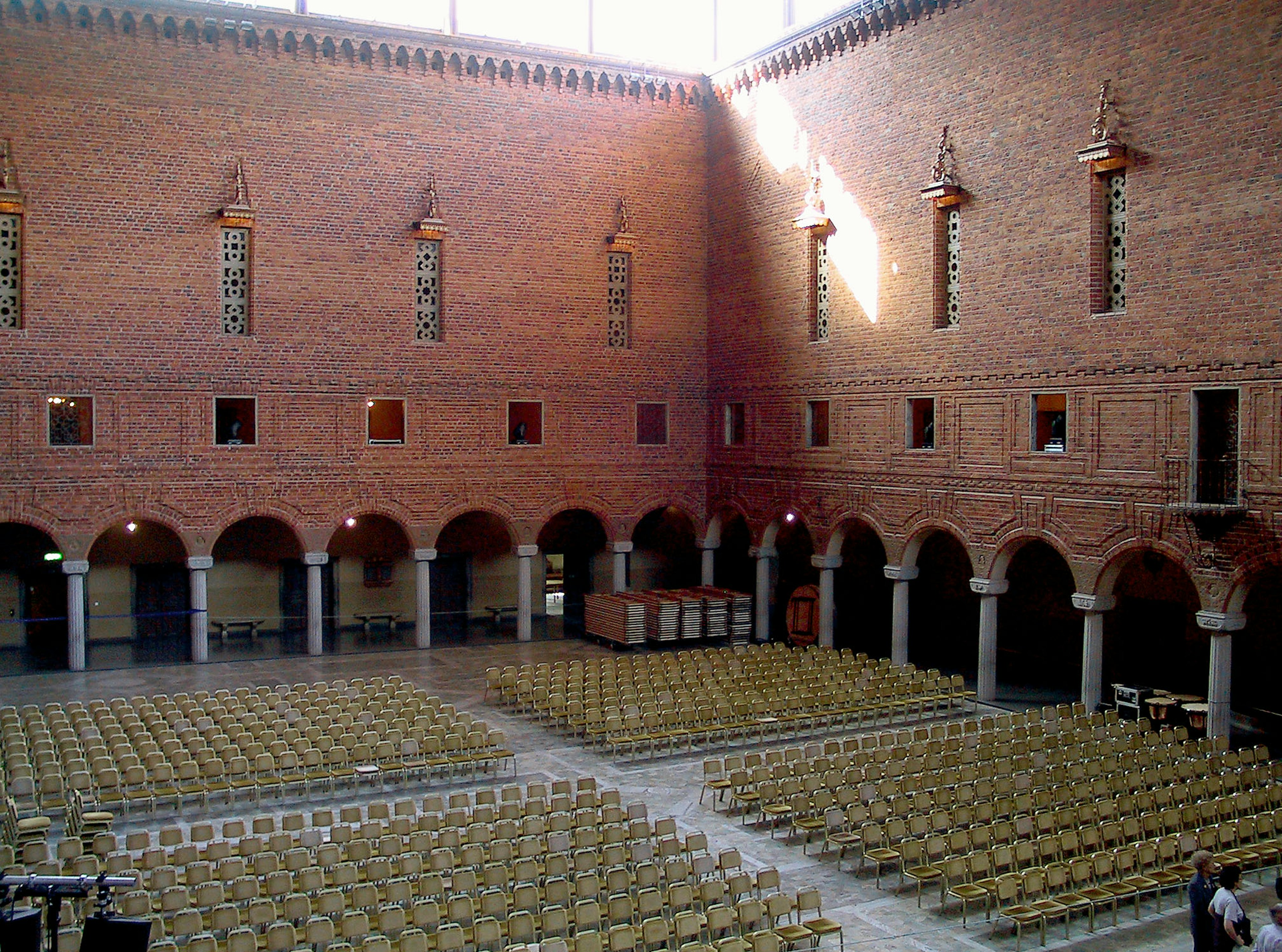 Vista interior del gran salón del Ayuntamiento de Estocolmo con asientos ordenados paredes de ladrillo rojo y columnas arqueadas