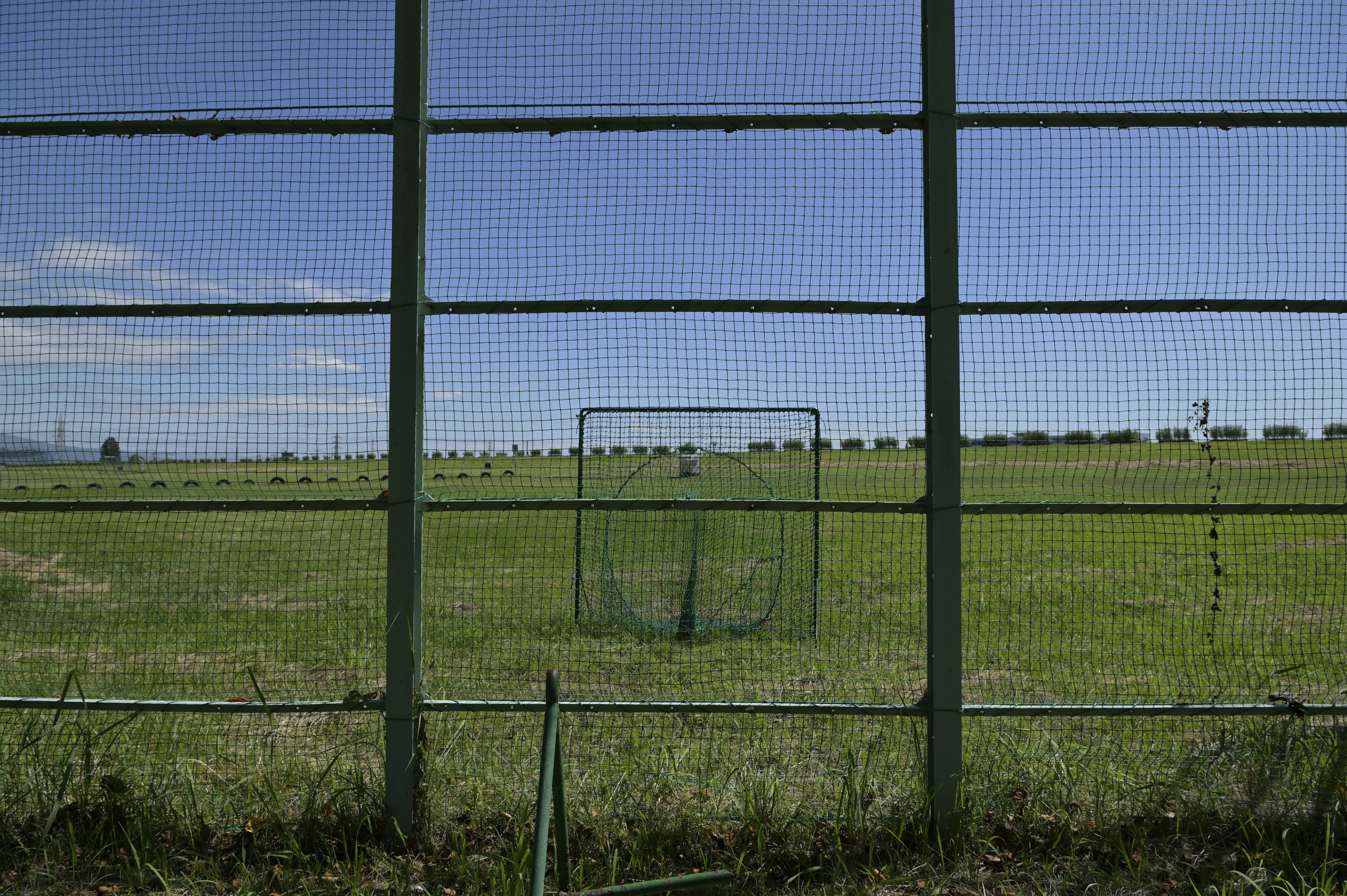 A green fence enclosing a wide grassy field under a blue sky