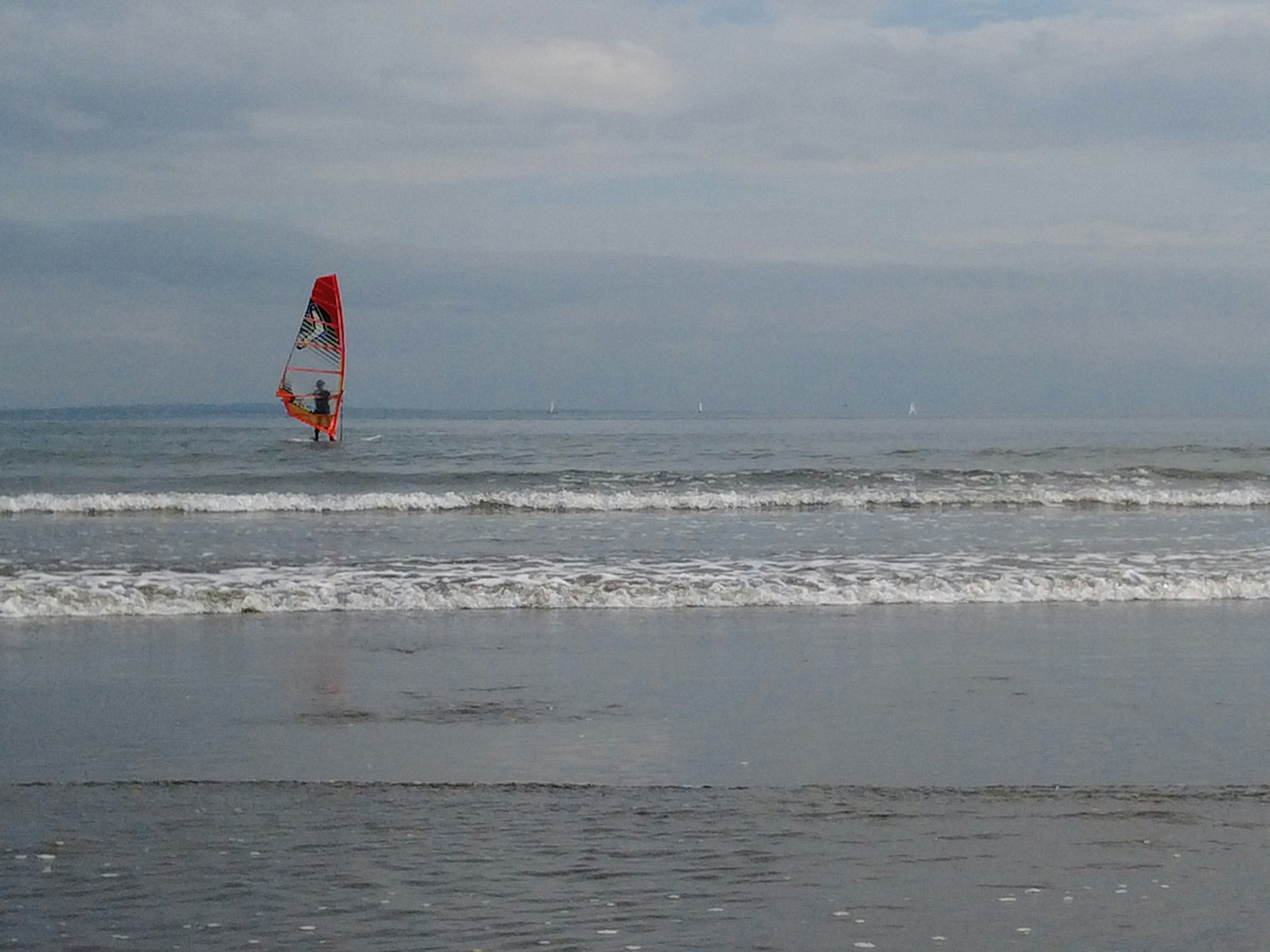 Personne faisant du windsurf sur l'océan avec une voile rouge et des vagues calmes