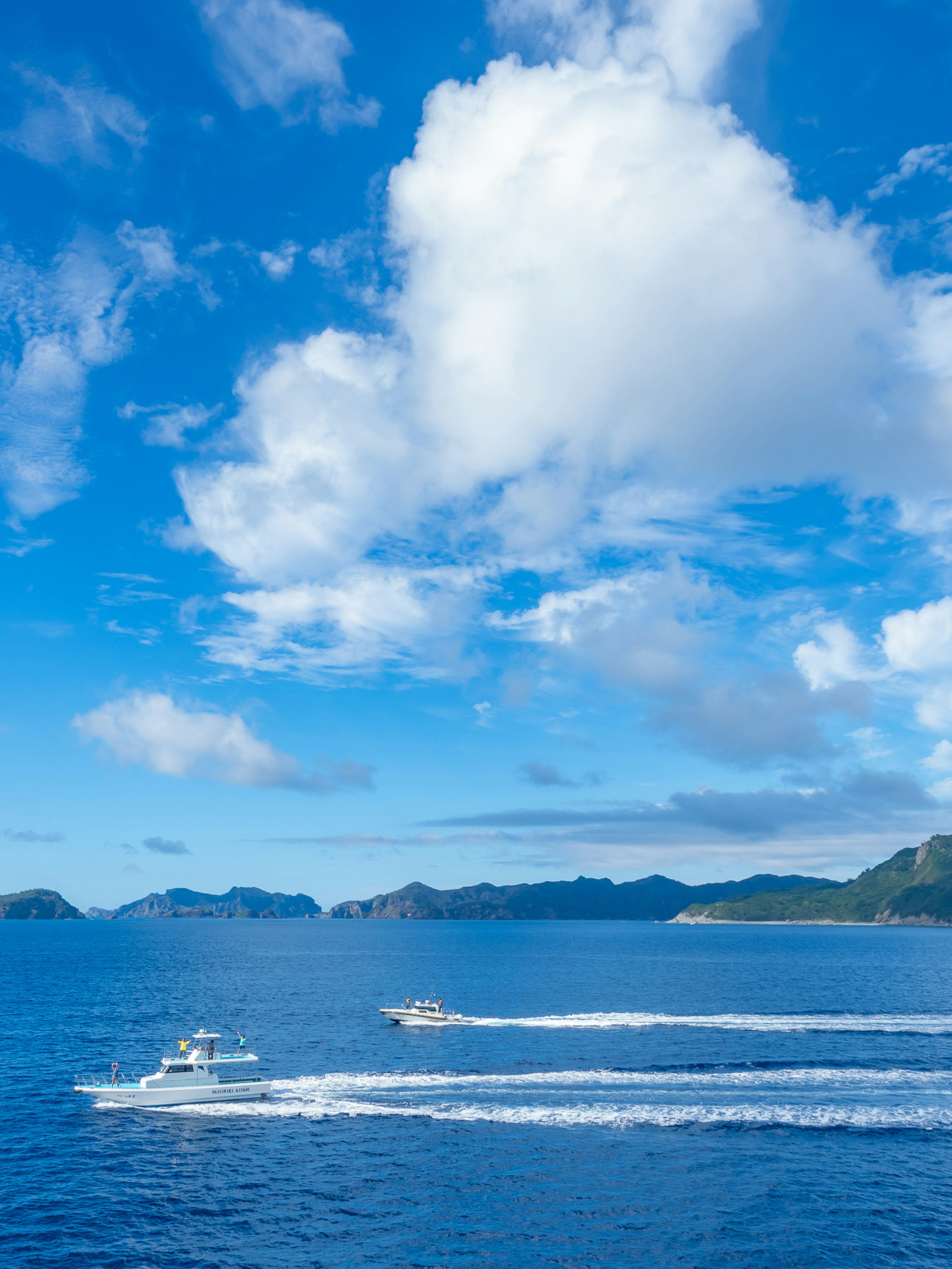 Una vista mozzafiato di mare e cielo blu con nuvole bianche e soffici e barche che creano onde