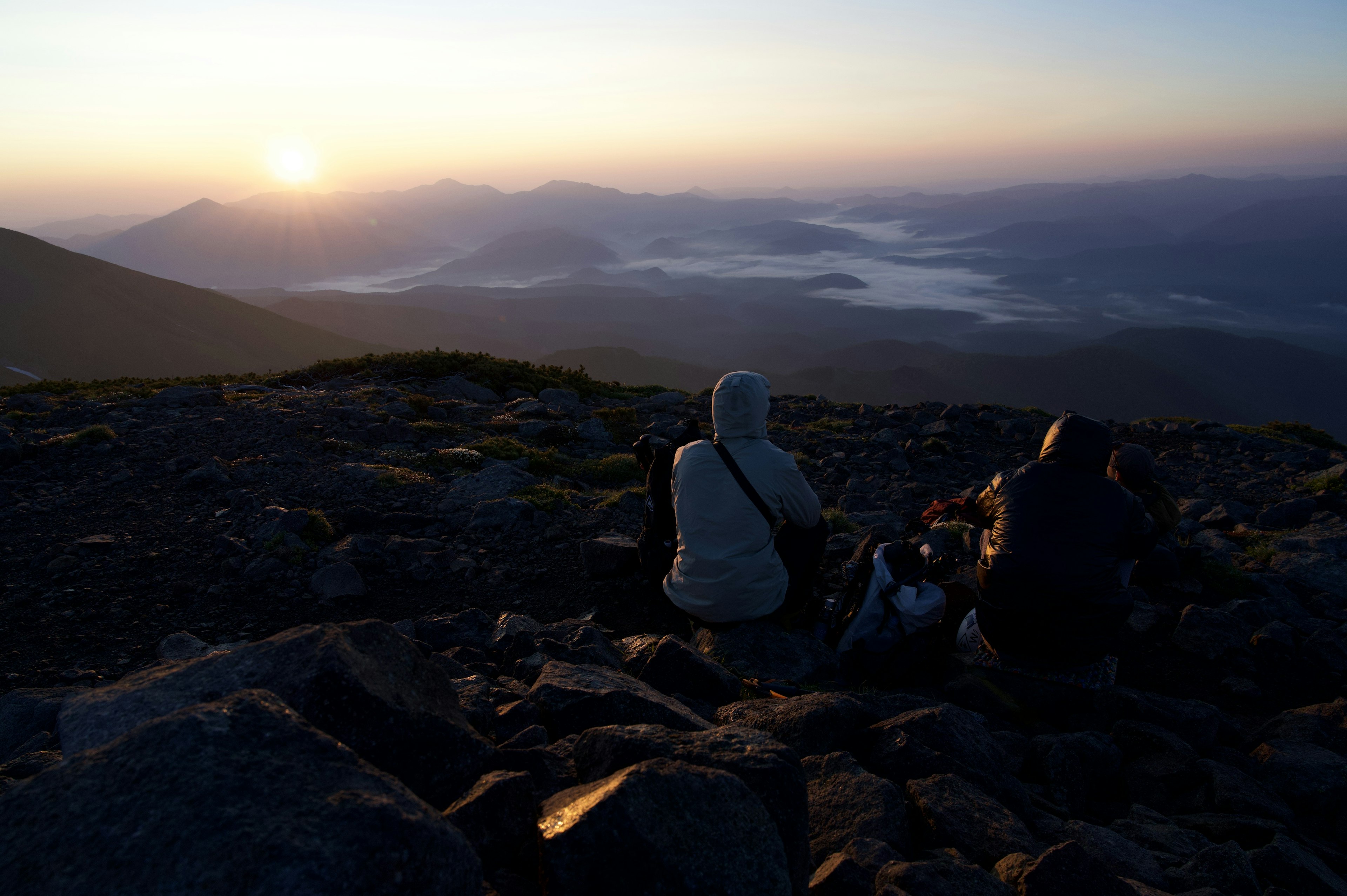 Zwei Wanderer beobachten den Sonnenaufgang von einem Berggipfel mit einem nebligen Tal im Hintergrund