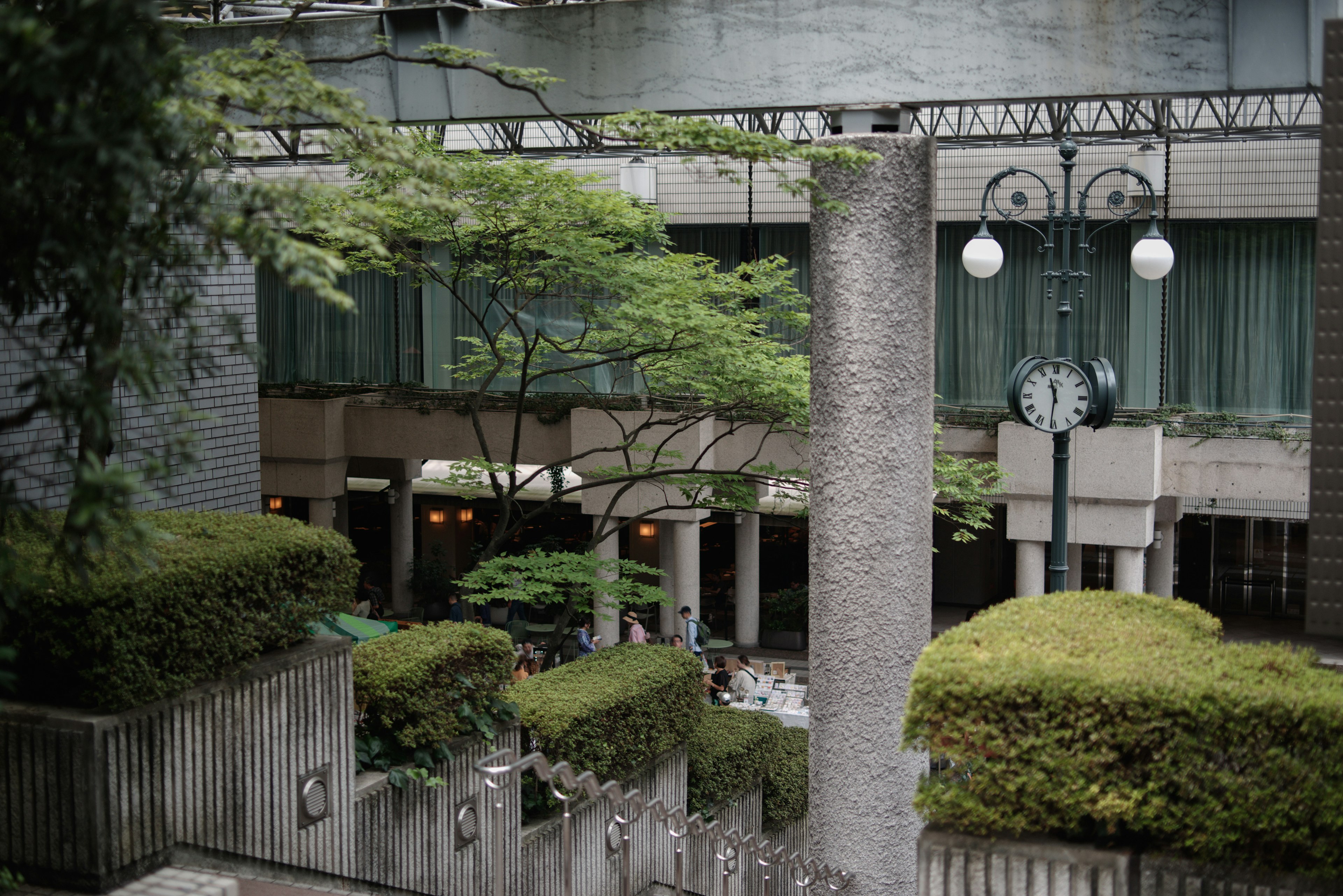 A scene showing a cafe surrounded by green trees and neatly arranged shrubs