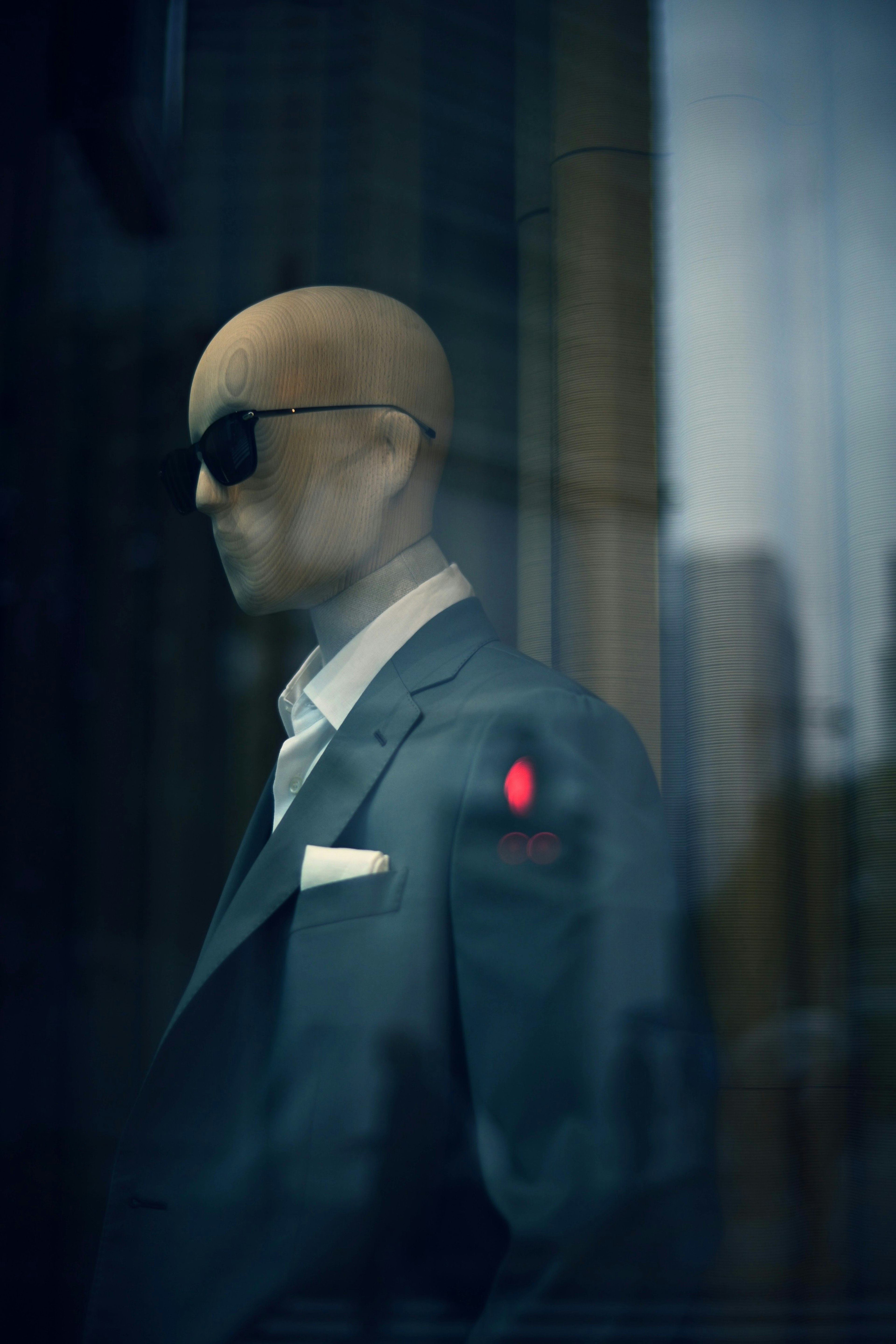 A mannequin dressed in a business suit wearing sunglasses stands still