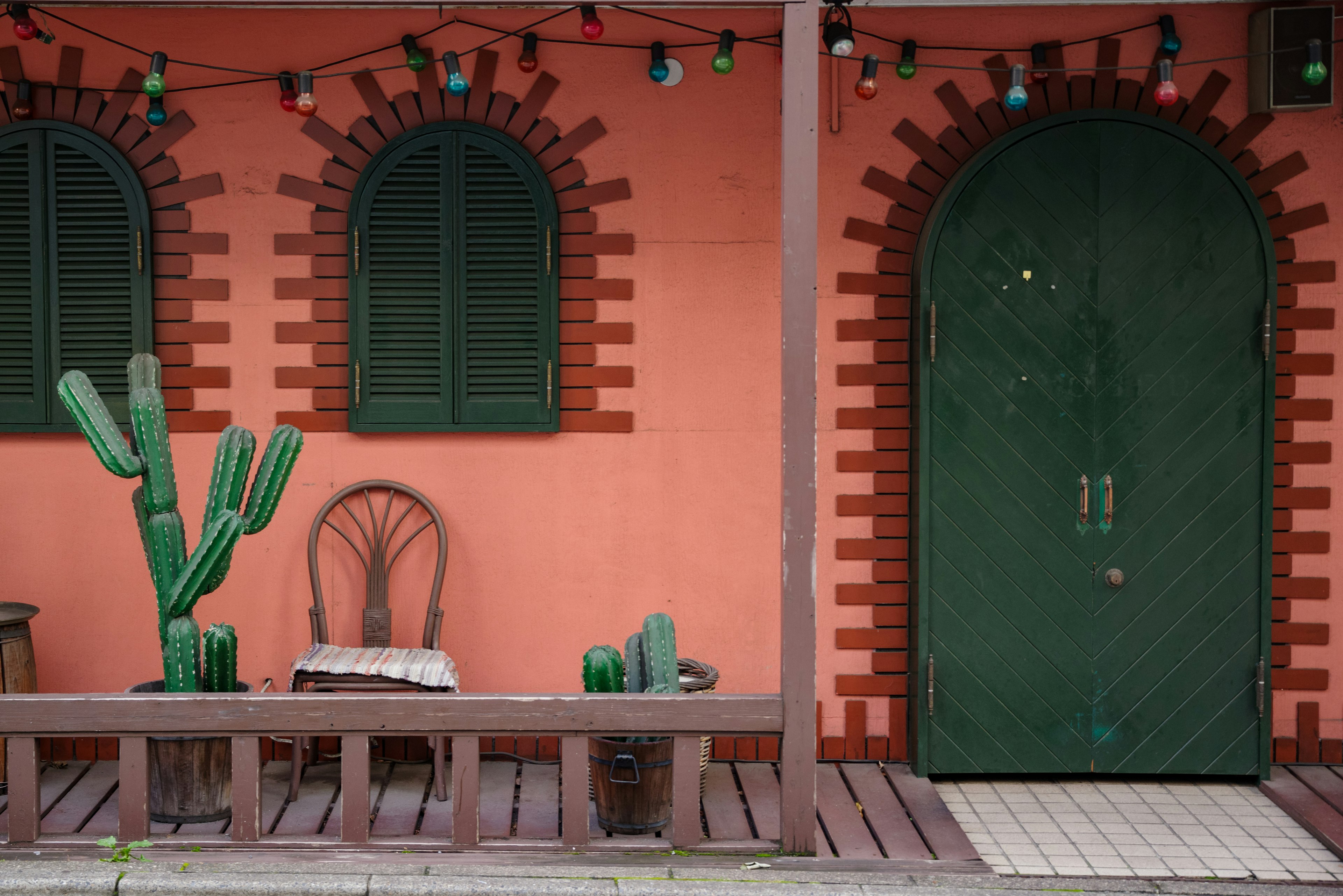 Extérieur coloré d'une maison avec une porte verte comprenant une chaise et des cactus sur un banc