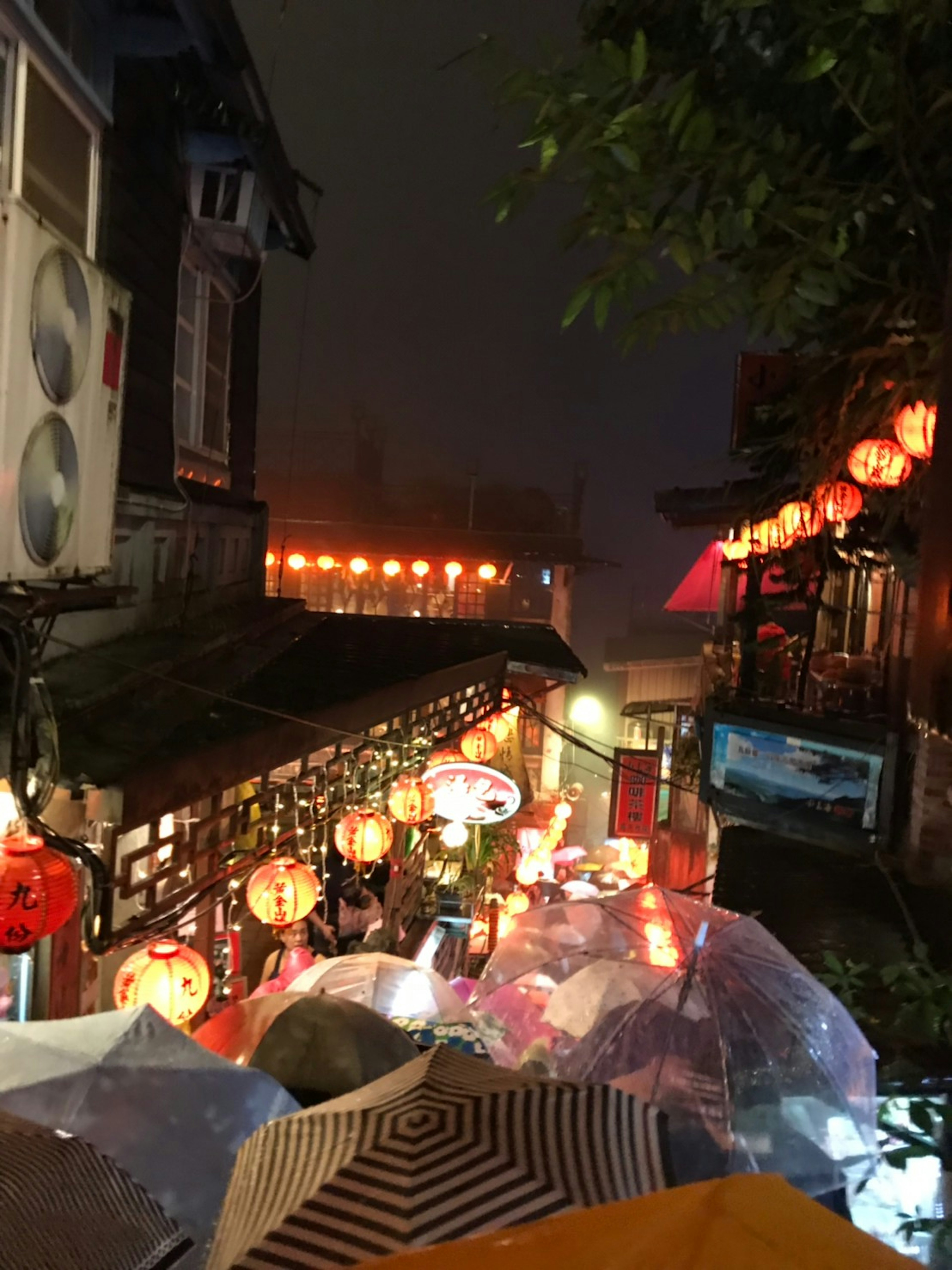 Street scene with lanterns glowing in the rain and umbrellas