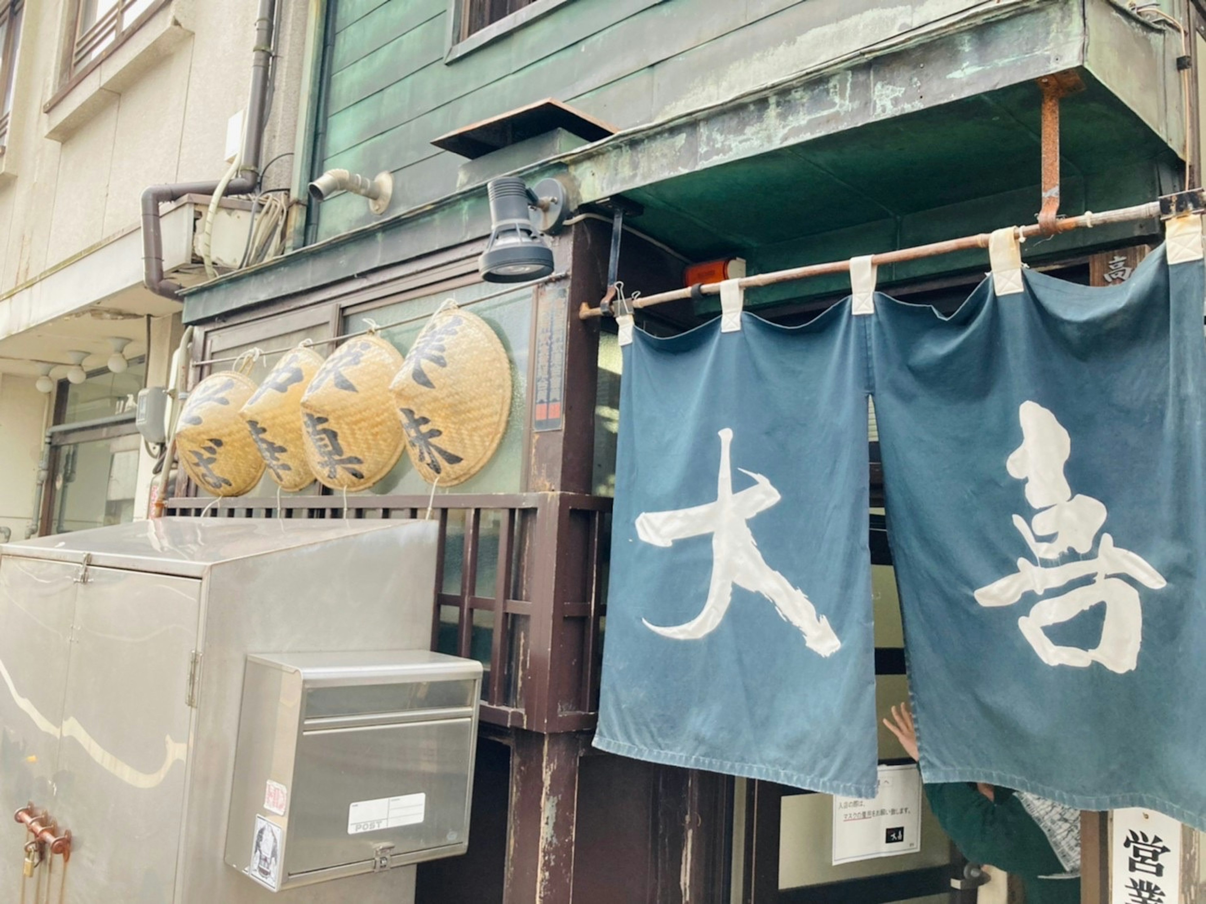 Exterior de un restaurante japonés con noren azul y letrero de madera