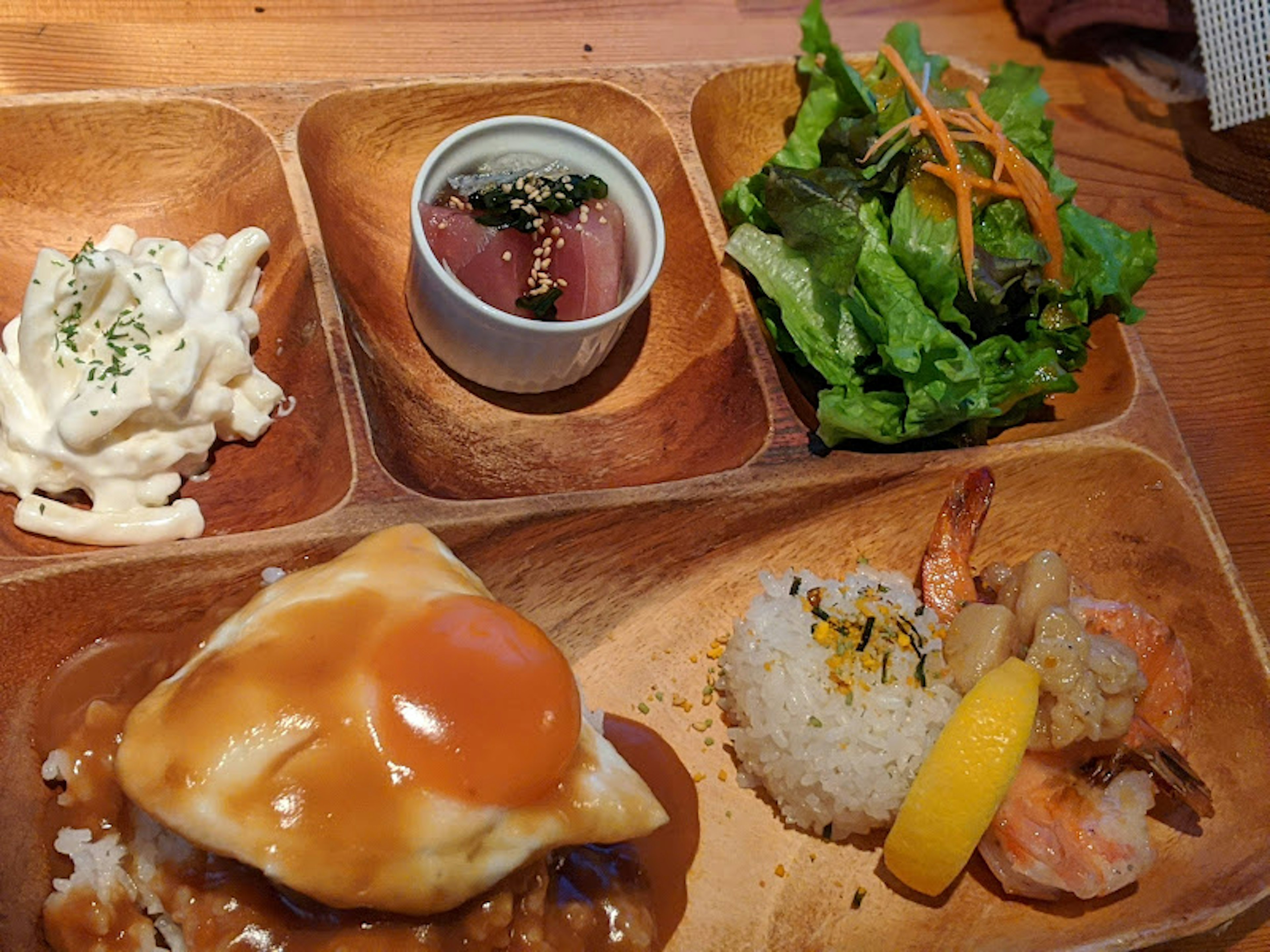 A platter featuring Japanese cuisine including rice with egg shrimp salad and tuna sashimi