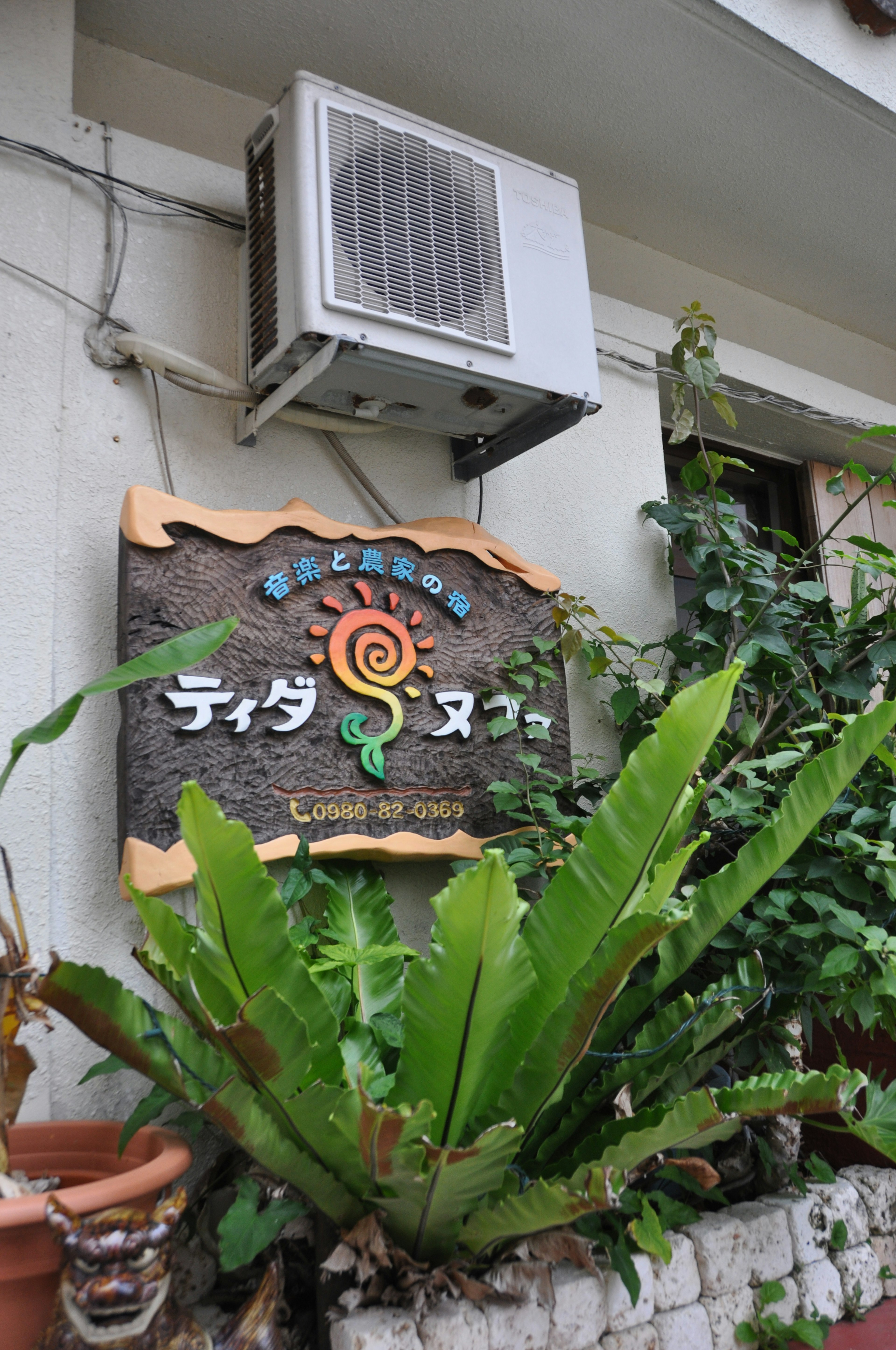 Tida Nuu sign mounted on a wall with an air conditioning unit and lush green plants