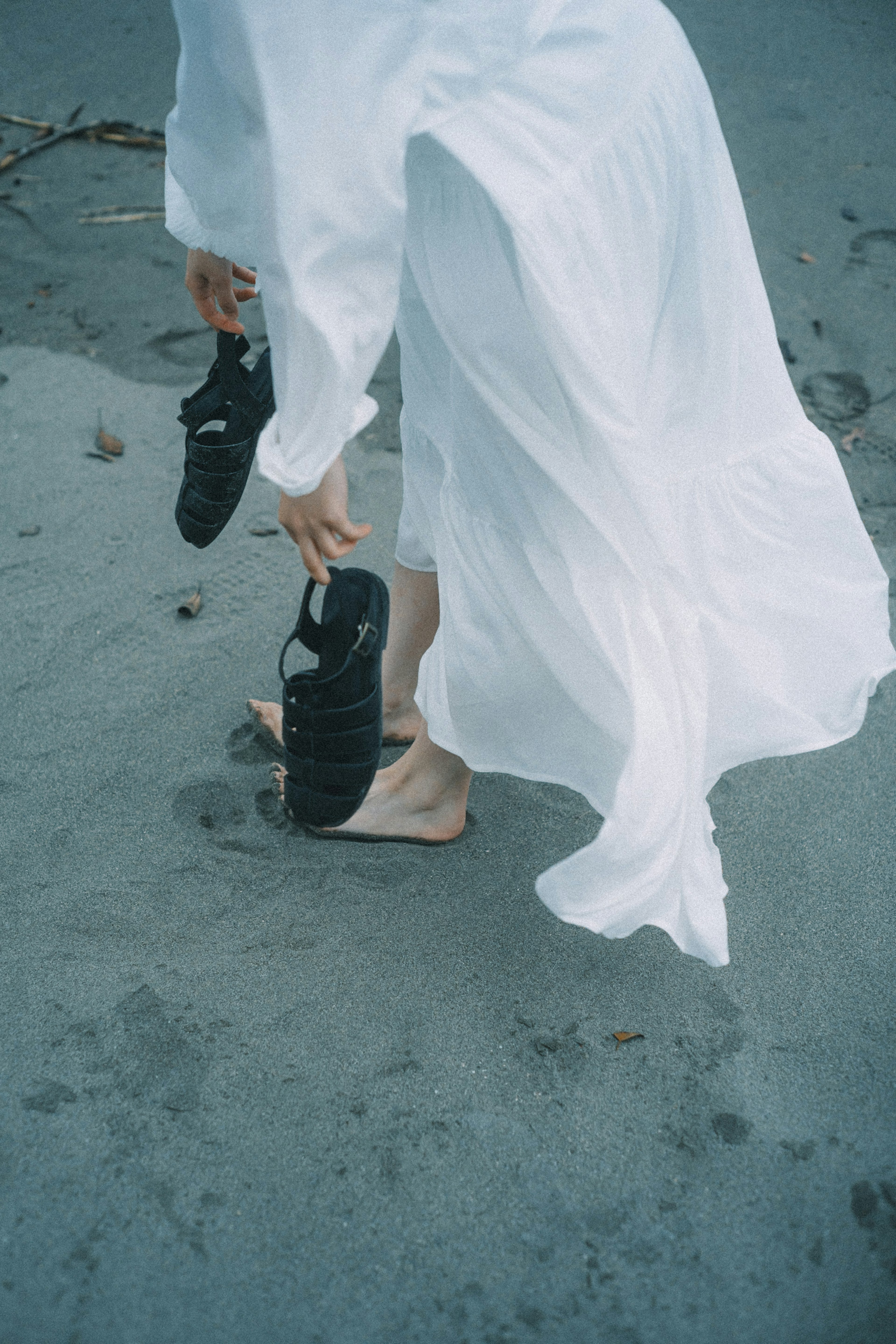 Wanita berpakaian putih memegang sepatu hitam di pantai