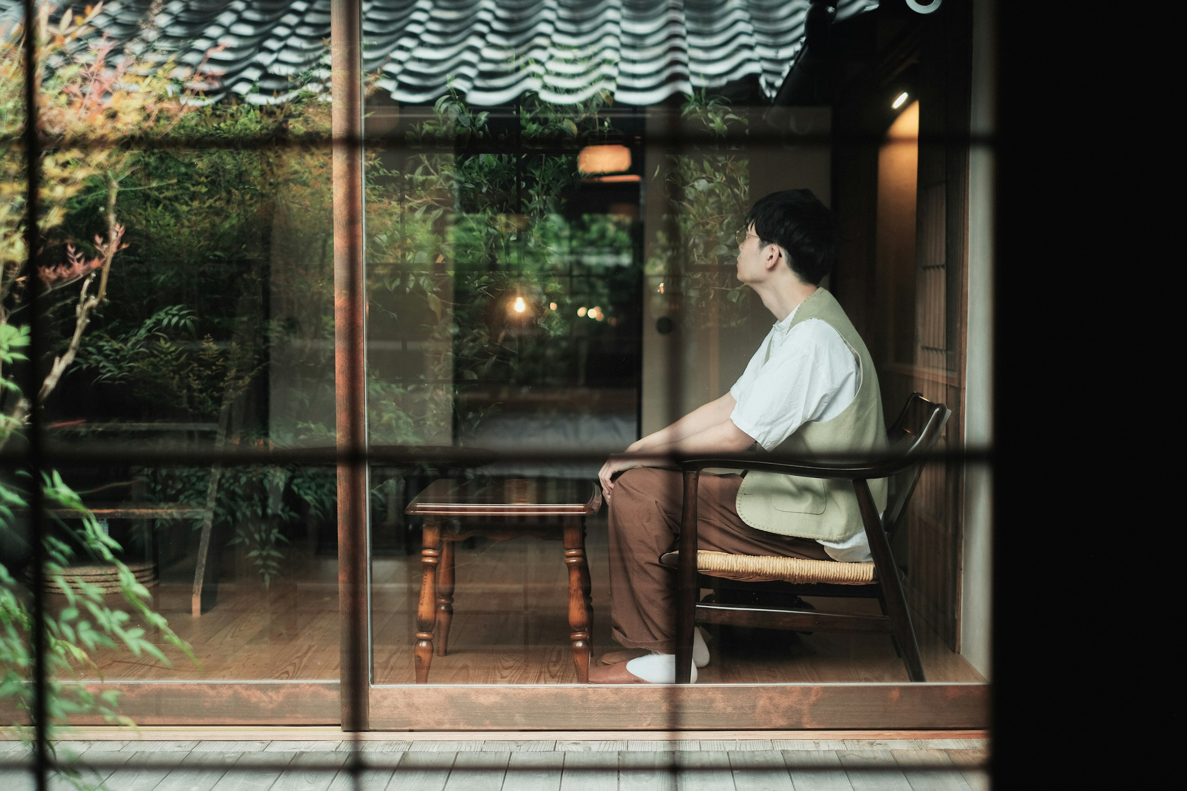 A man sitting in a traditional room gazing outside through a window with greenery