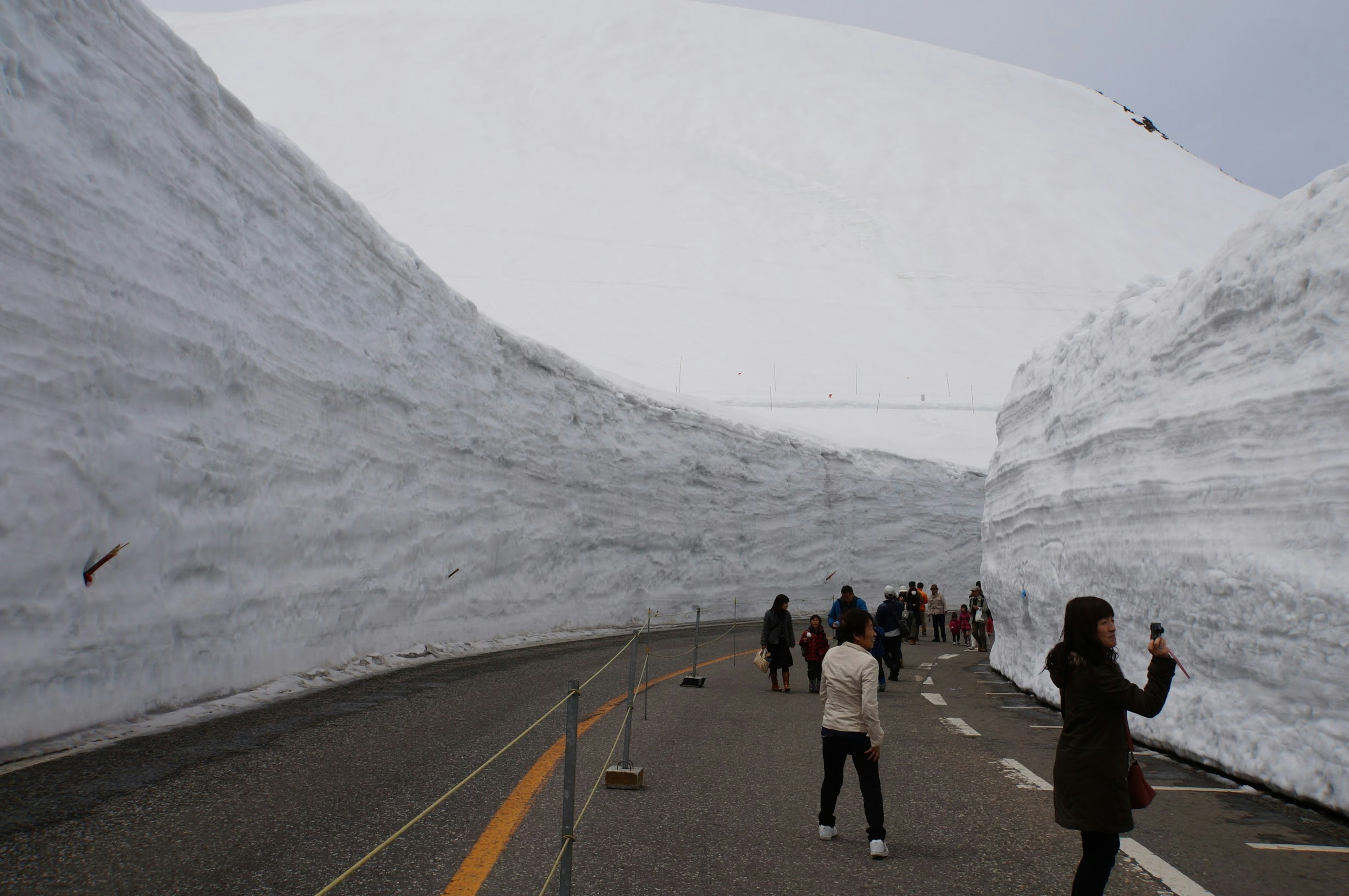 雪の壁に囲まれた道路を歩く観光客たち