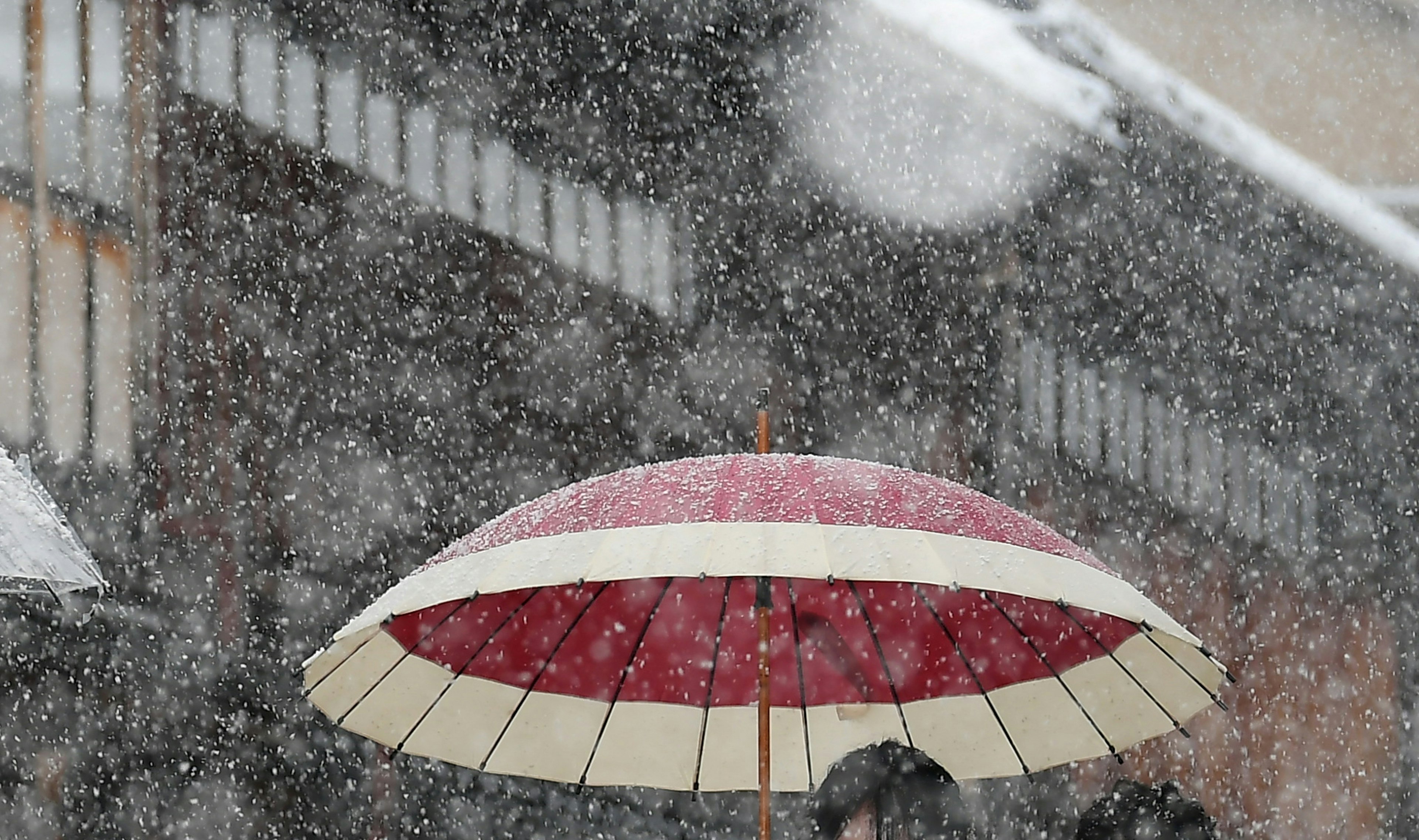 Una persona con un paraguas rojo y blanco en una tormenta de nieve