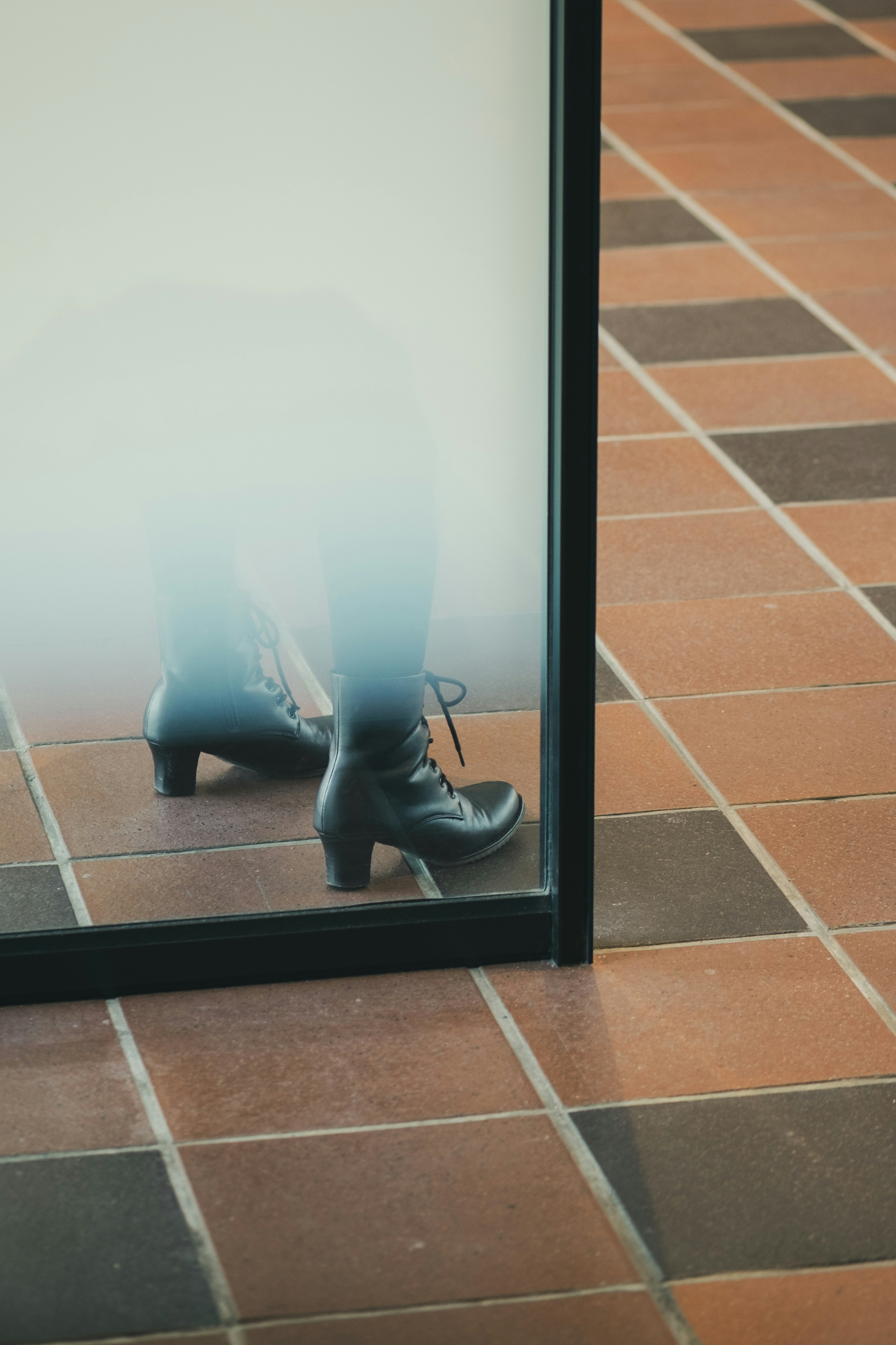 Zapato reflejado en una partición de vidrio con piso de baldosas