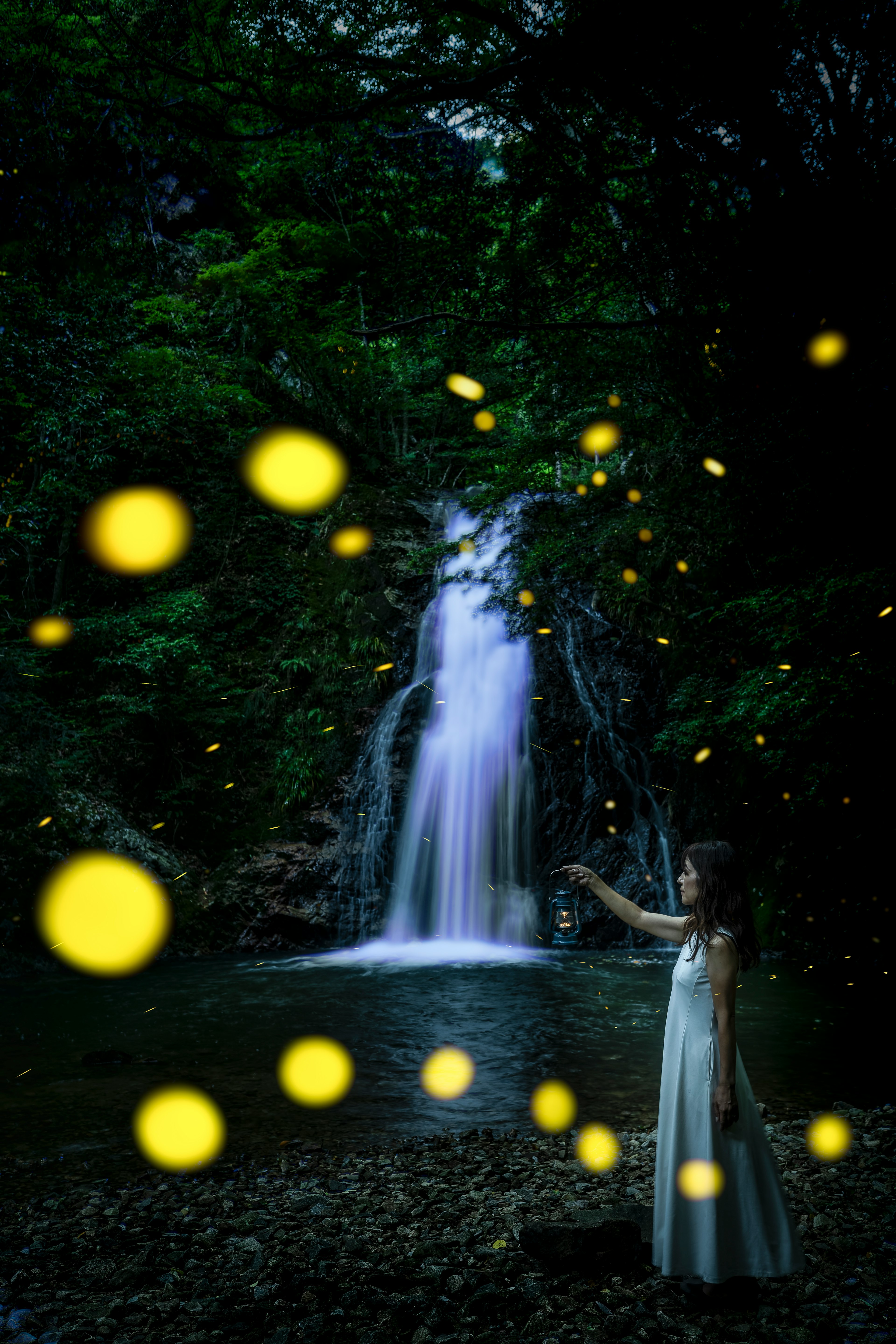 A girl in a white dress standing by a beautiful waterfall with glowing fireflies