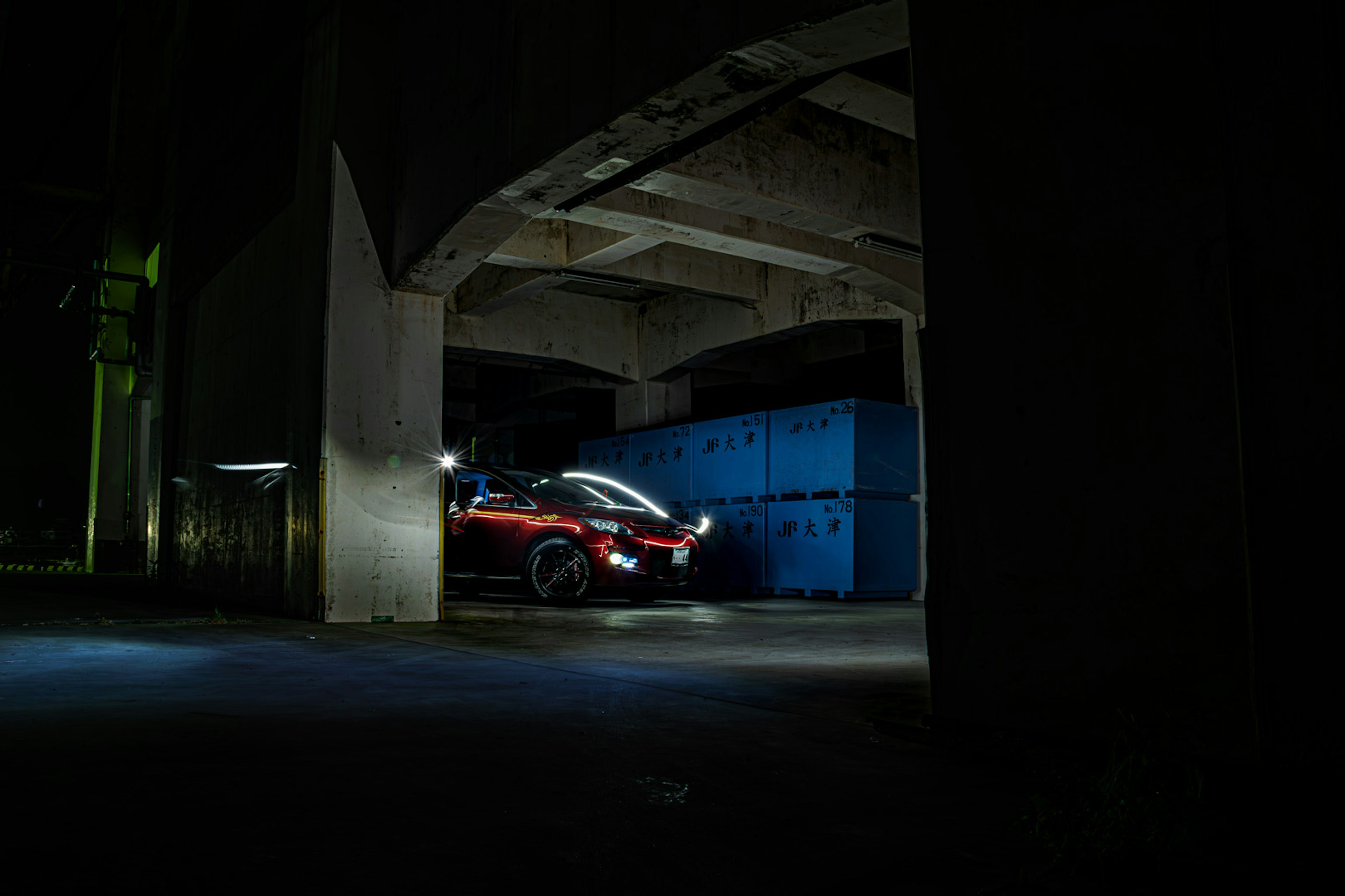 A red car parked in a dark area with a blue container