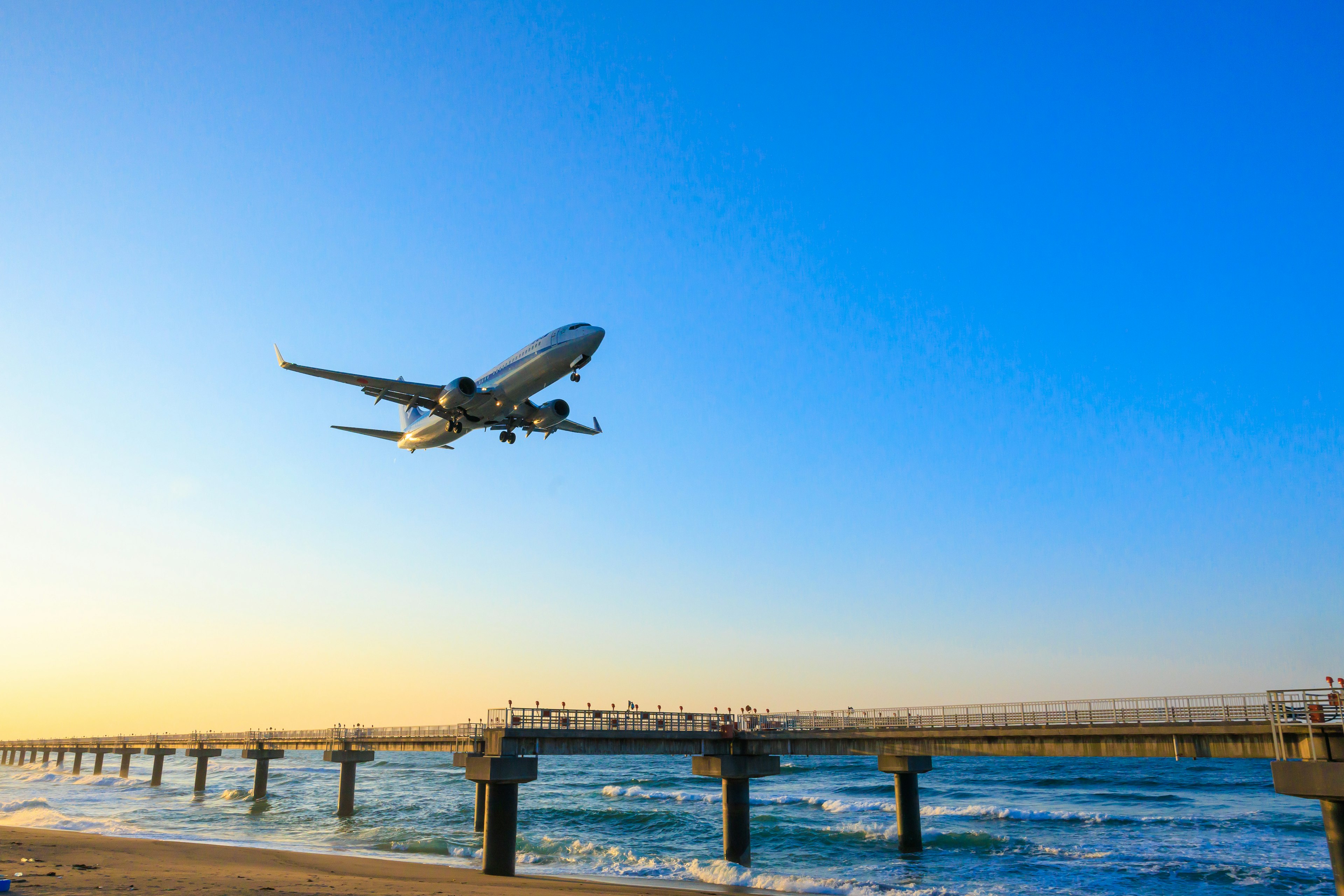 飛行機が青い空を背景に海上の桟橋の上を飛んでいる