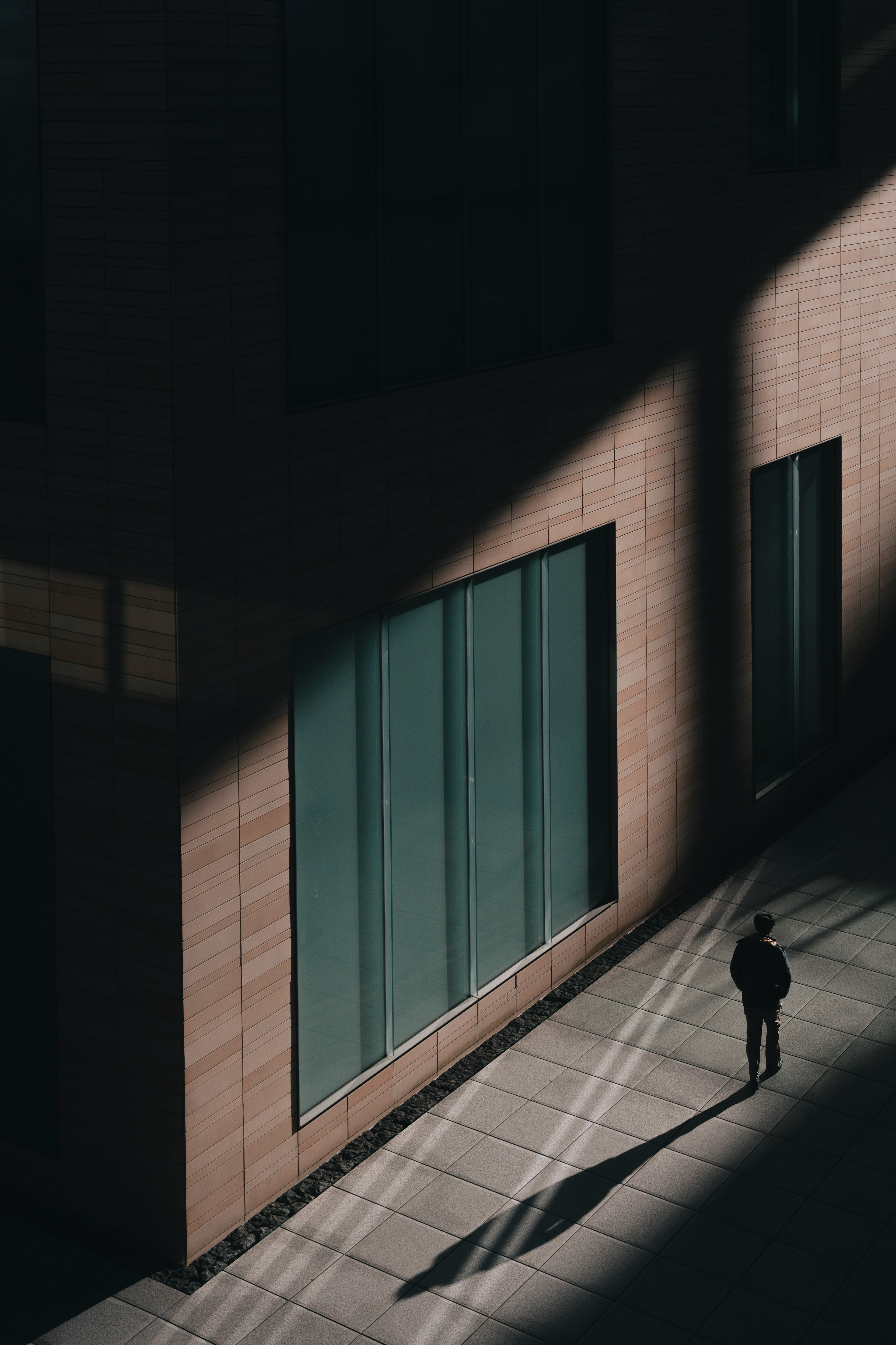 Eine Person steht im Schatten neben einem modernen Gebäude mit großen Fenstern