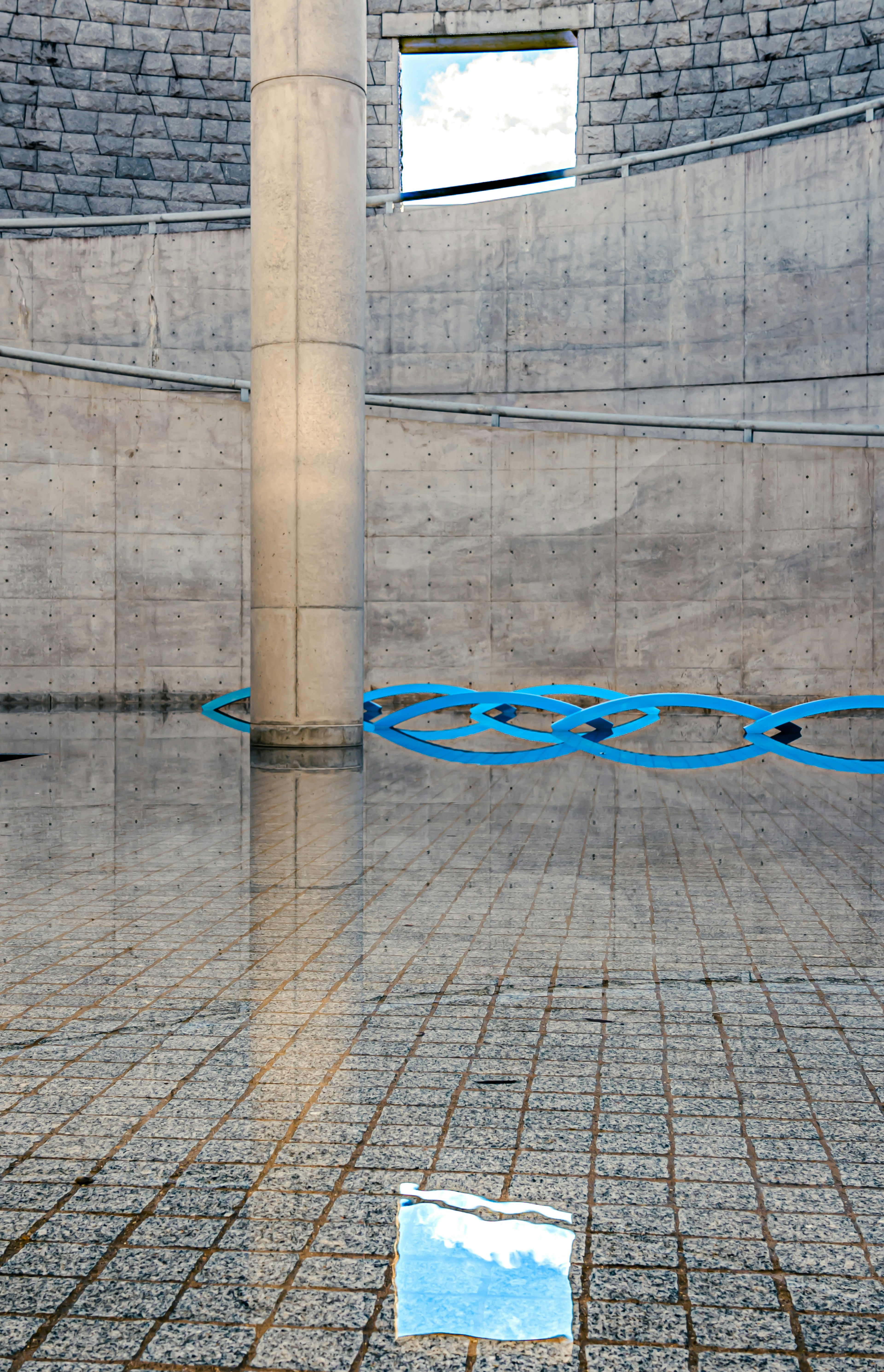 Espacio moderno con pilar de concreto y reflejo del cielo azul en el agua