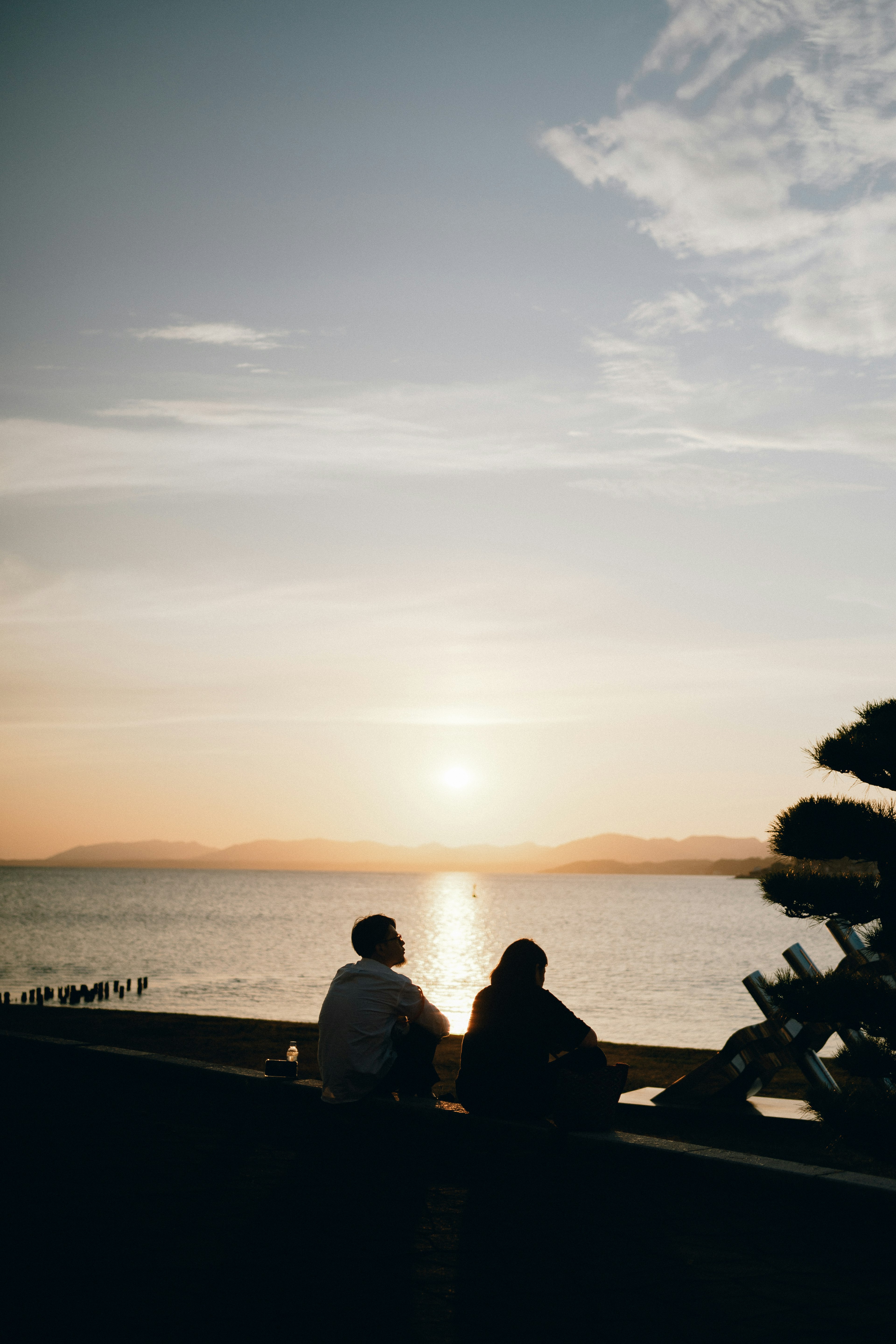 Silhouette von zwei Personen, die den Sonnenuntergang über einem ruhigen Meer betrachten