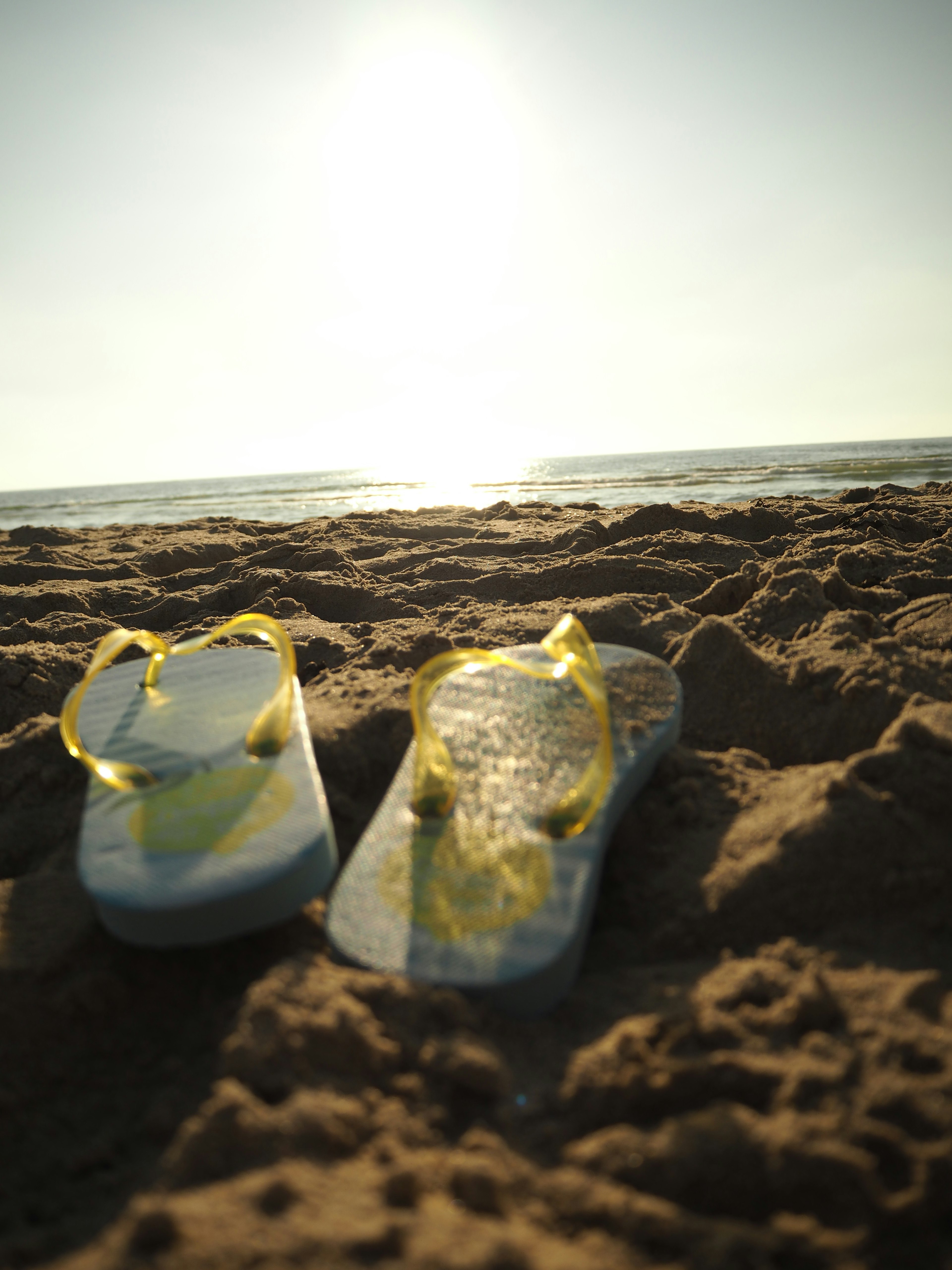 Yellow flip flops on sandy beach with ocean in the background