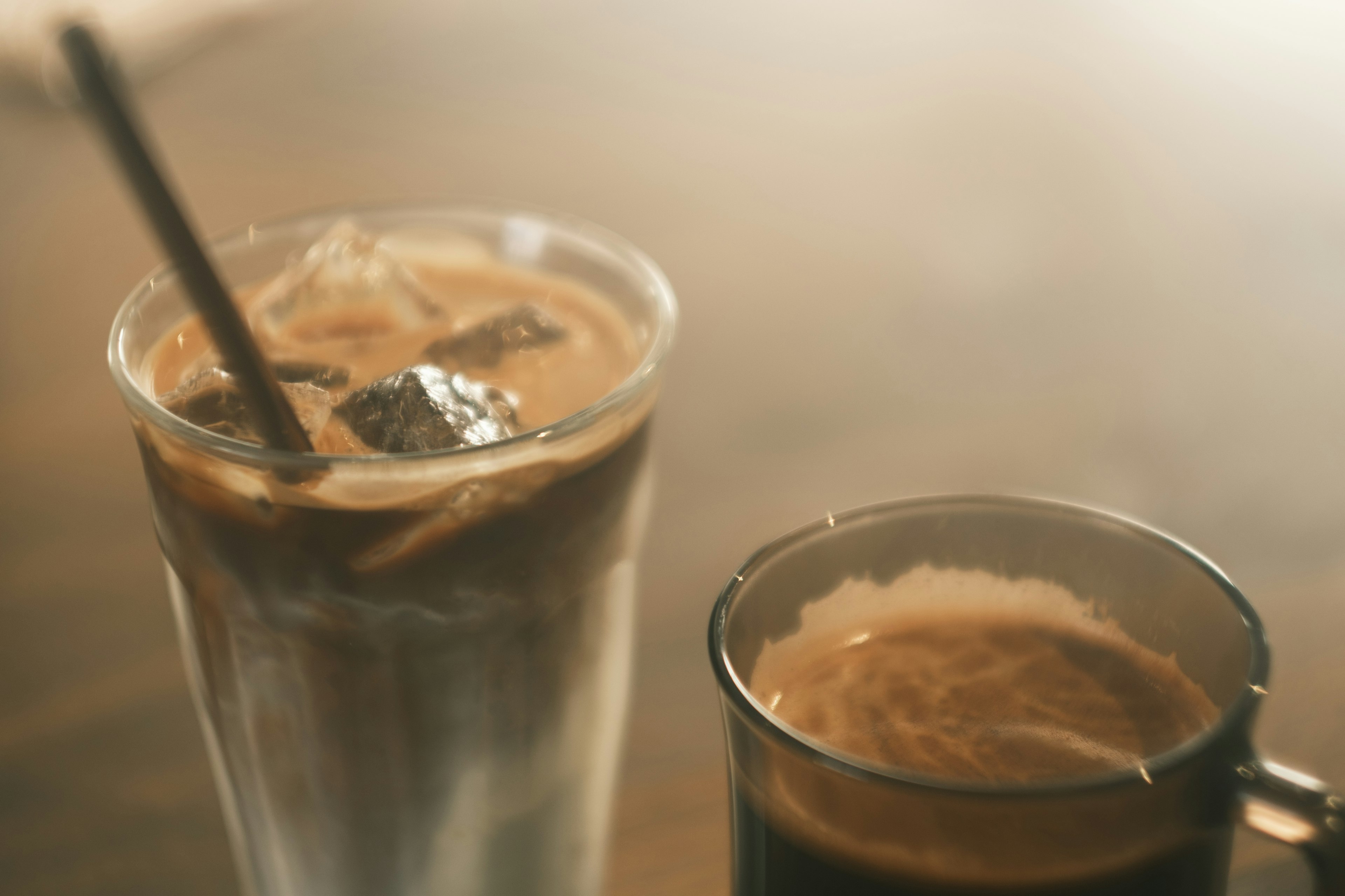 Un vaso de café helado con cubitos de hielo y una taza de café caliente sobre una mesa de madera