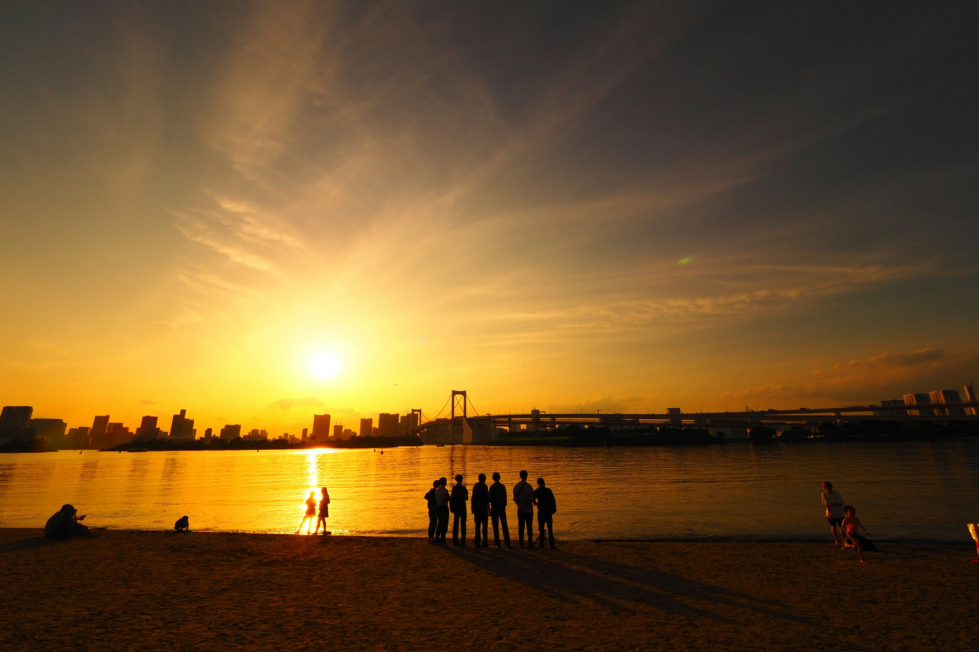 Silhouette de personnes au bord de la mer contre un coucher de soleil et un horizon urbain