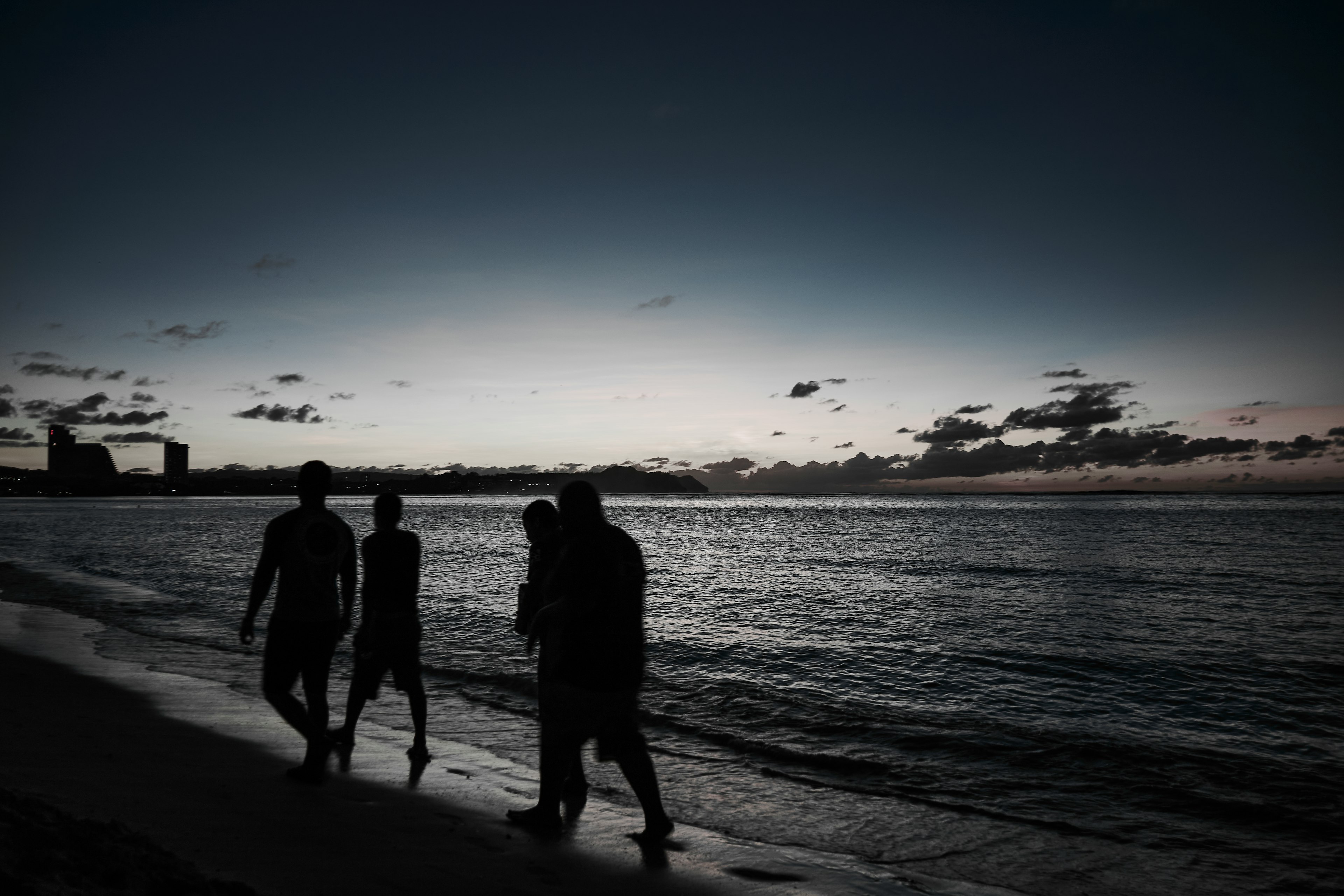 Siluetas de personas caminando por la playa al anochecer