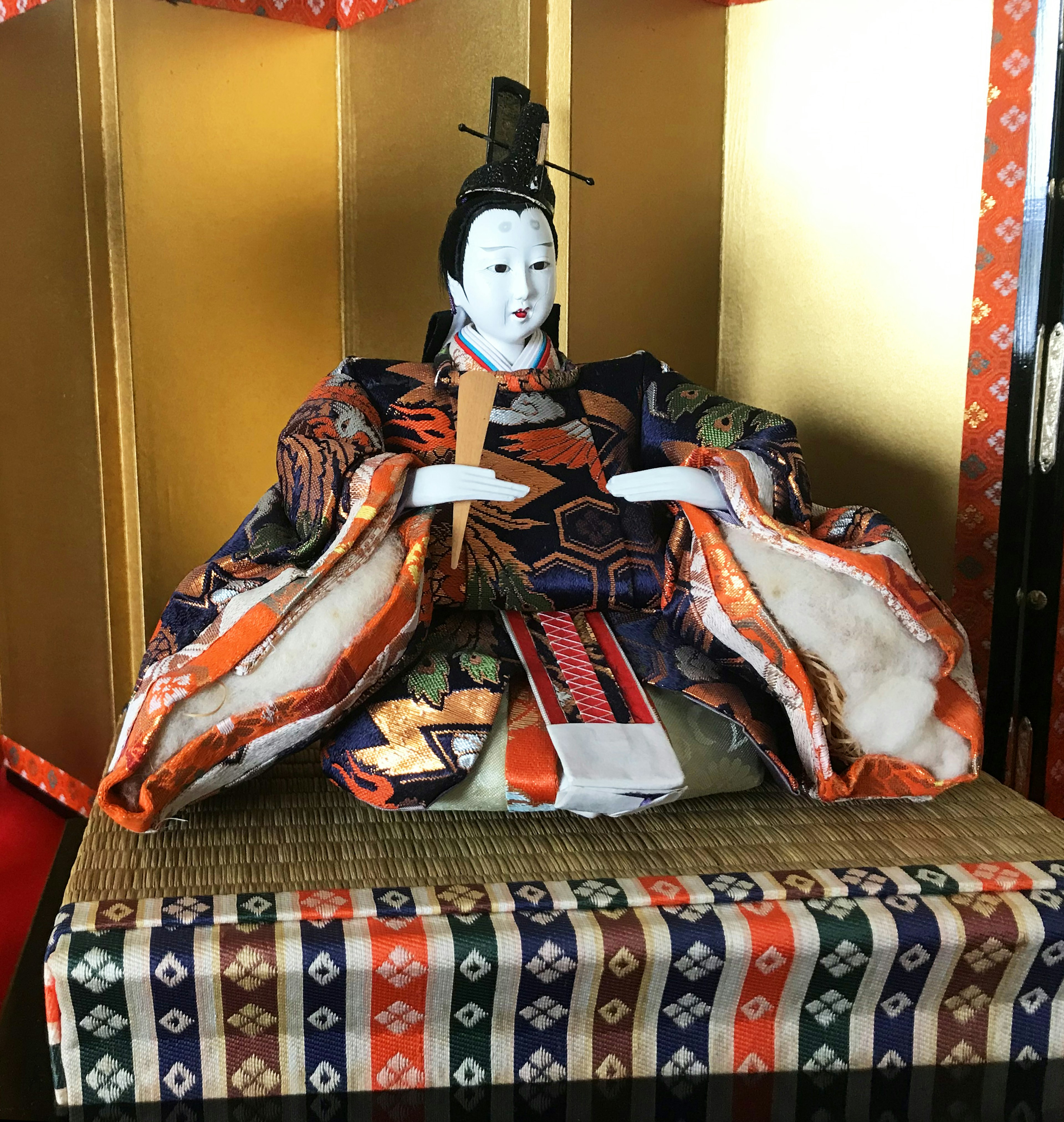 Traditional Japanese doll seated against a gold background