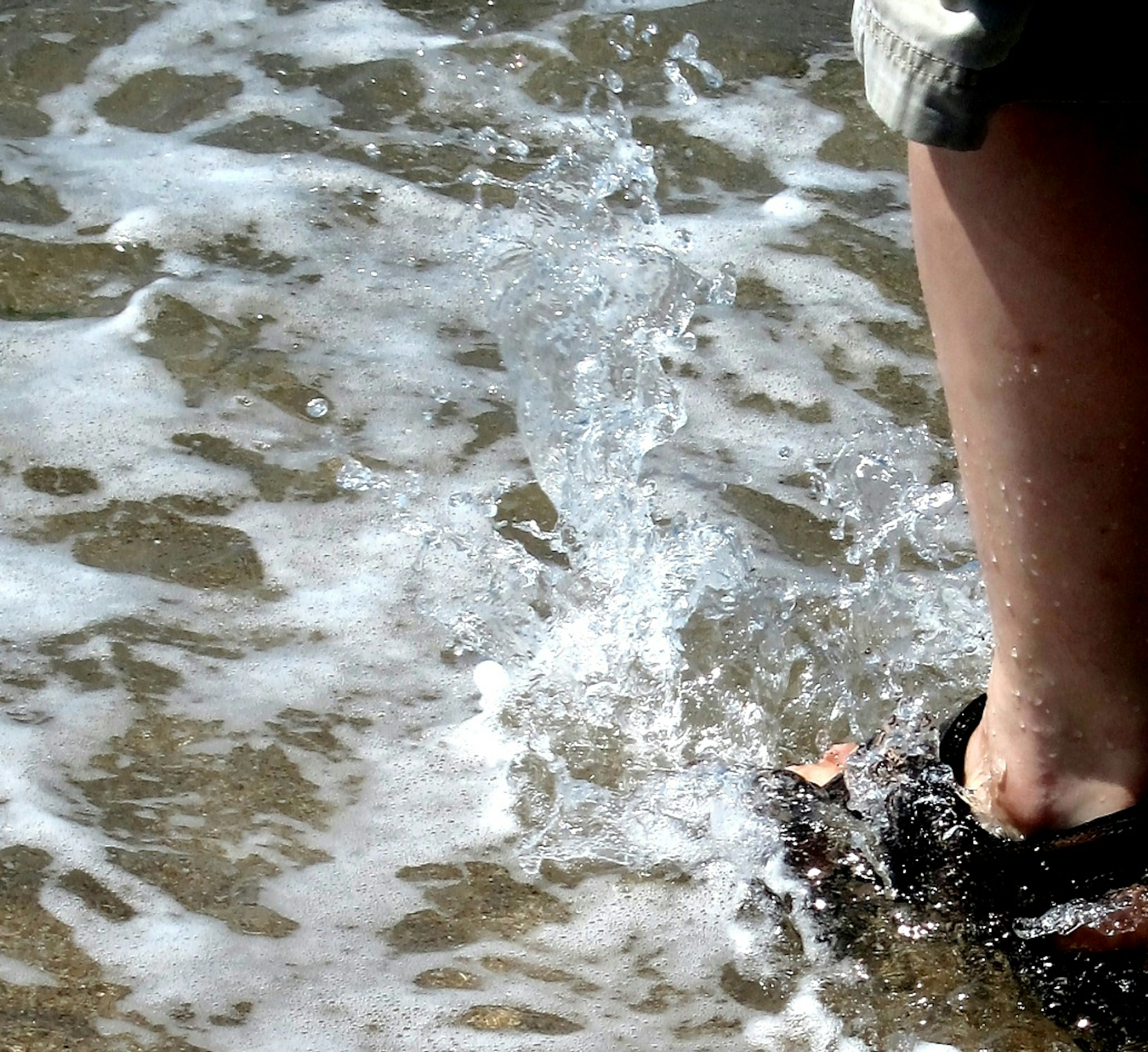 Füße spritzen in flachem Wasser am Strand