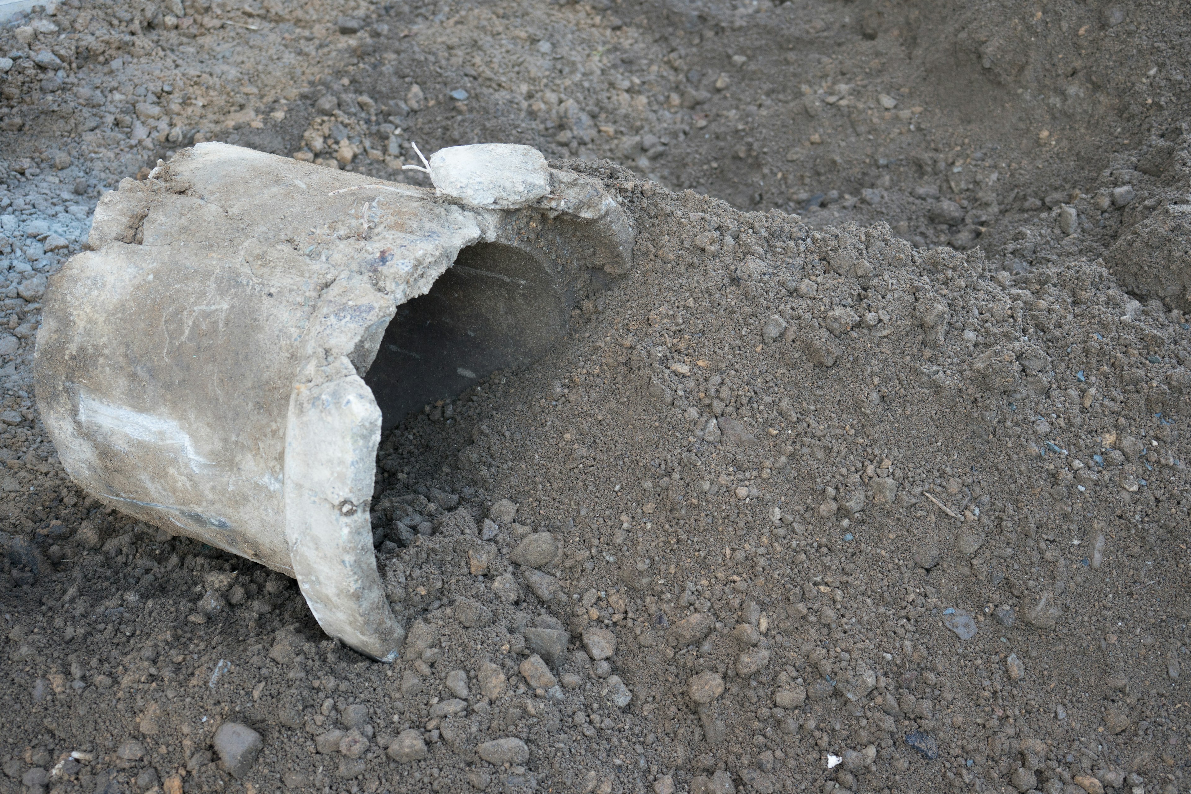 Damaged concrete pipe partially buried in dirt with surrounding soil