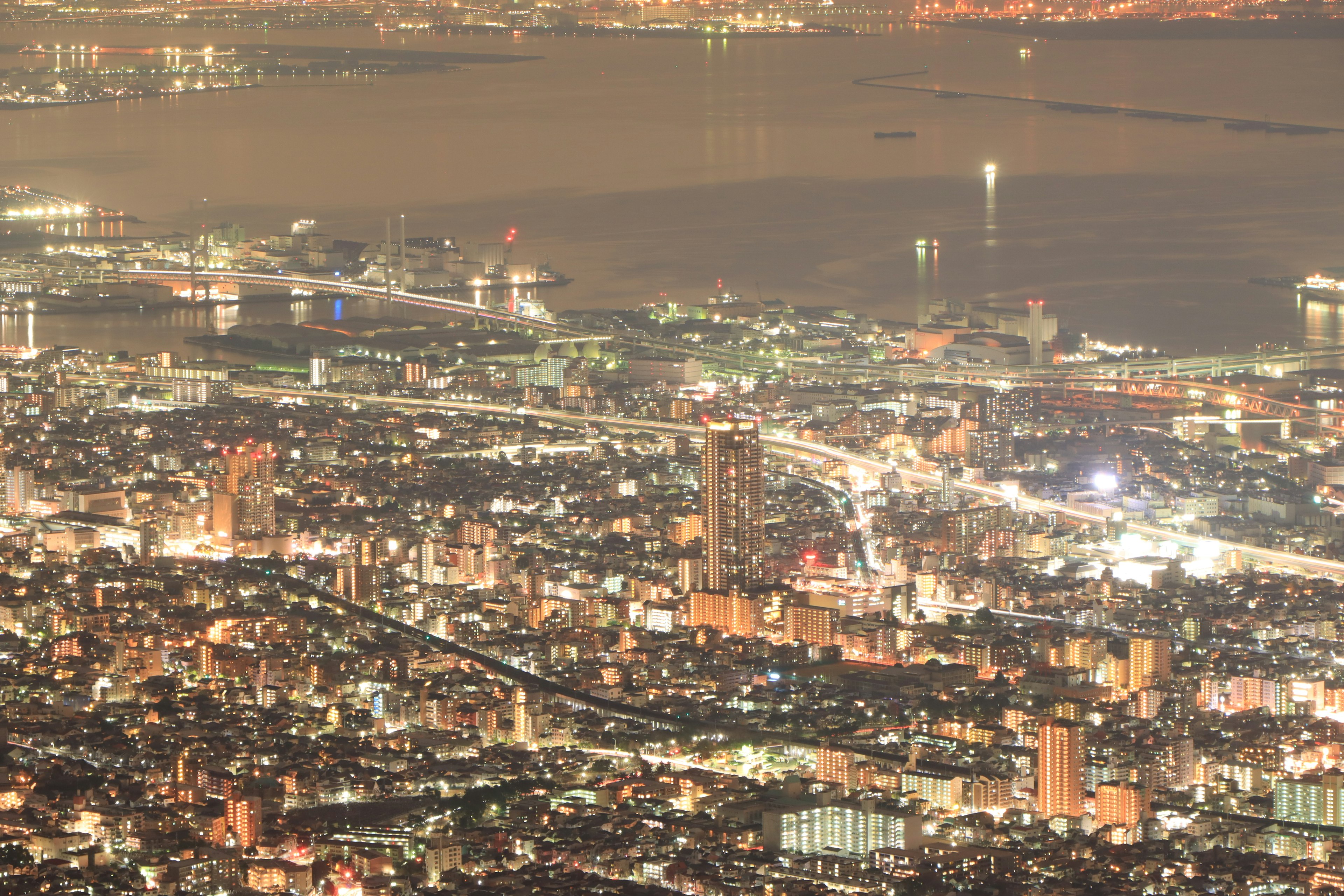 夜景の都市のパノラマ　海の近くの明るい建物　輝く街灯と交通の流れ