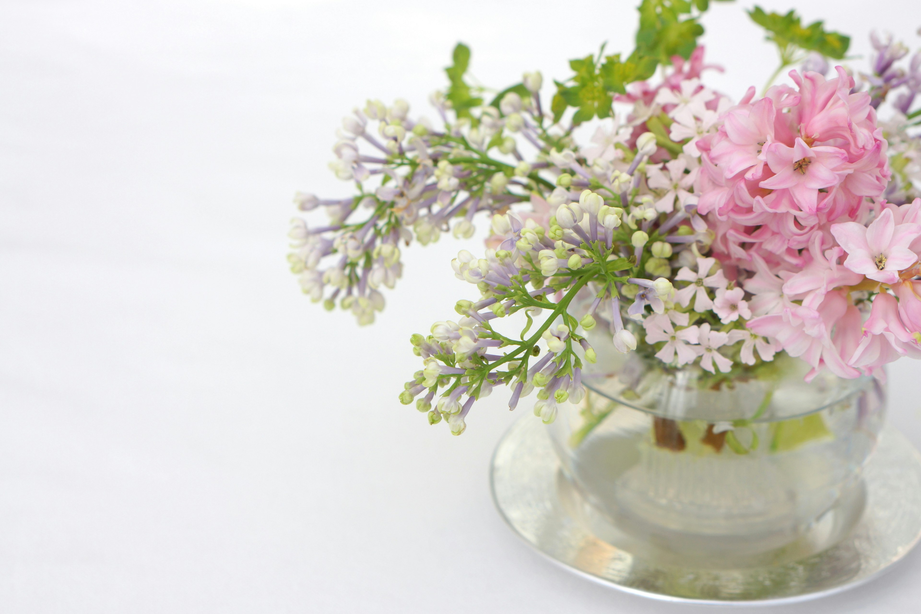 Un ramo de flores rosas y blancas con hojas verdes en un jarrón transparente