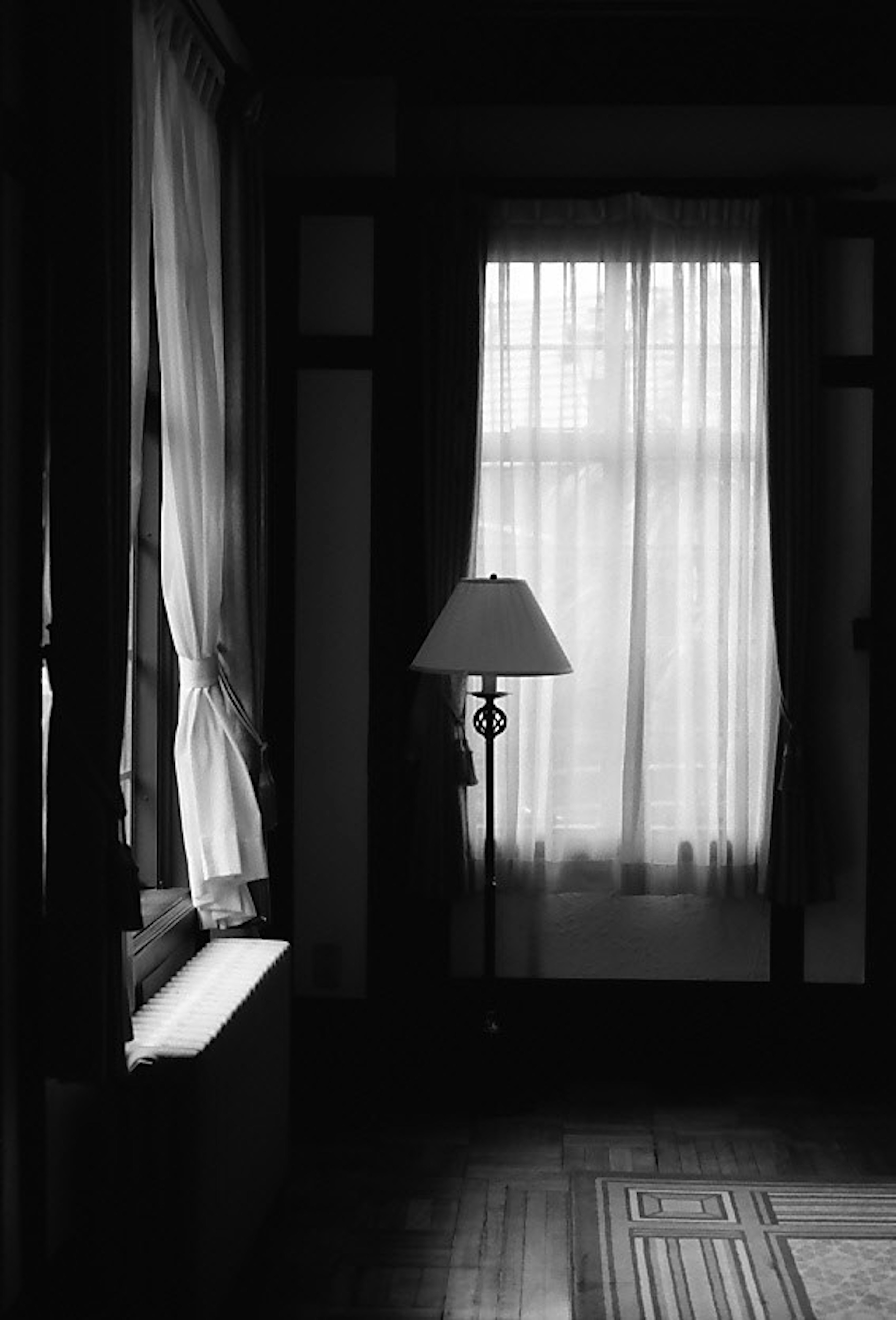 Black and white interior of a room featuring a window with curtains and a lamp