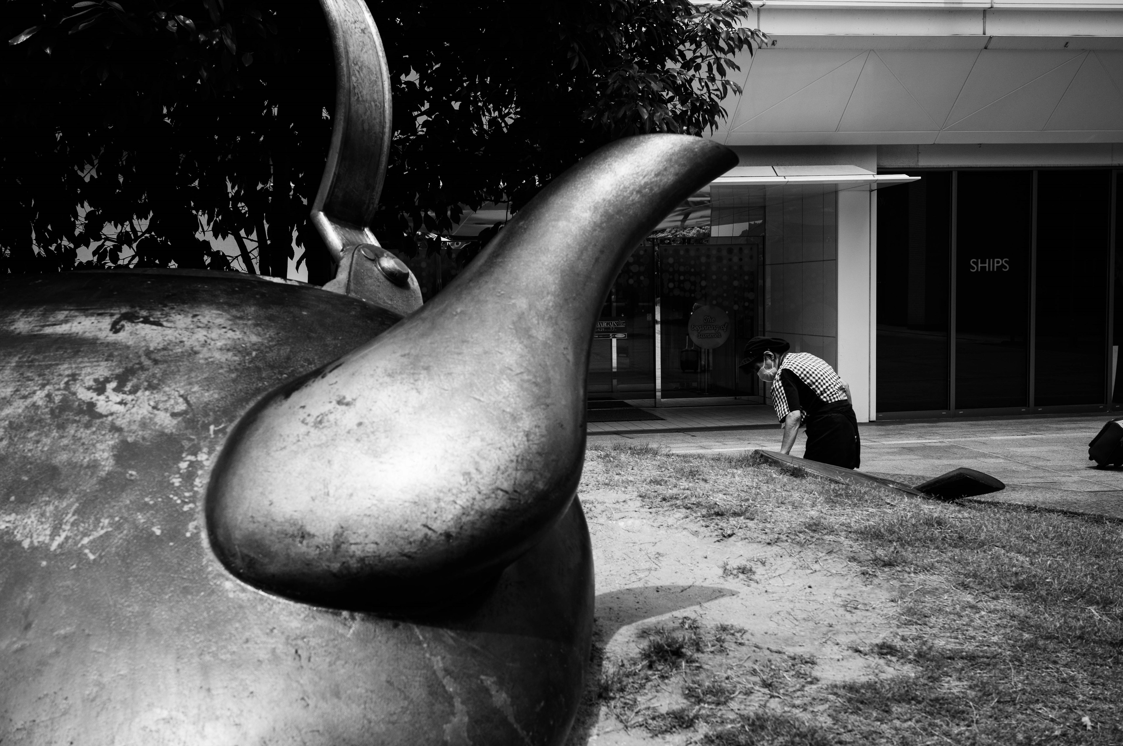 Black and white image of a large teapot and a person kneeling