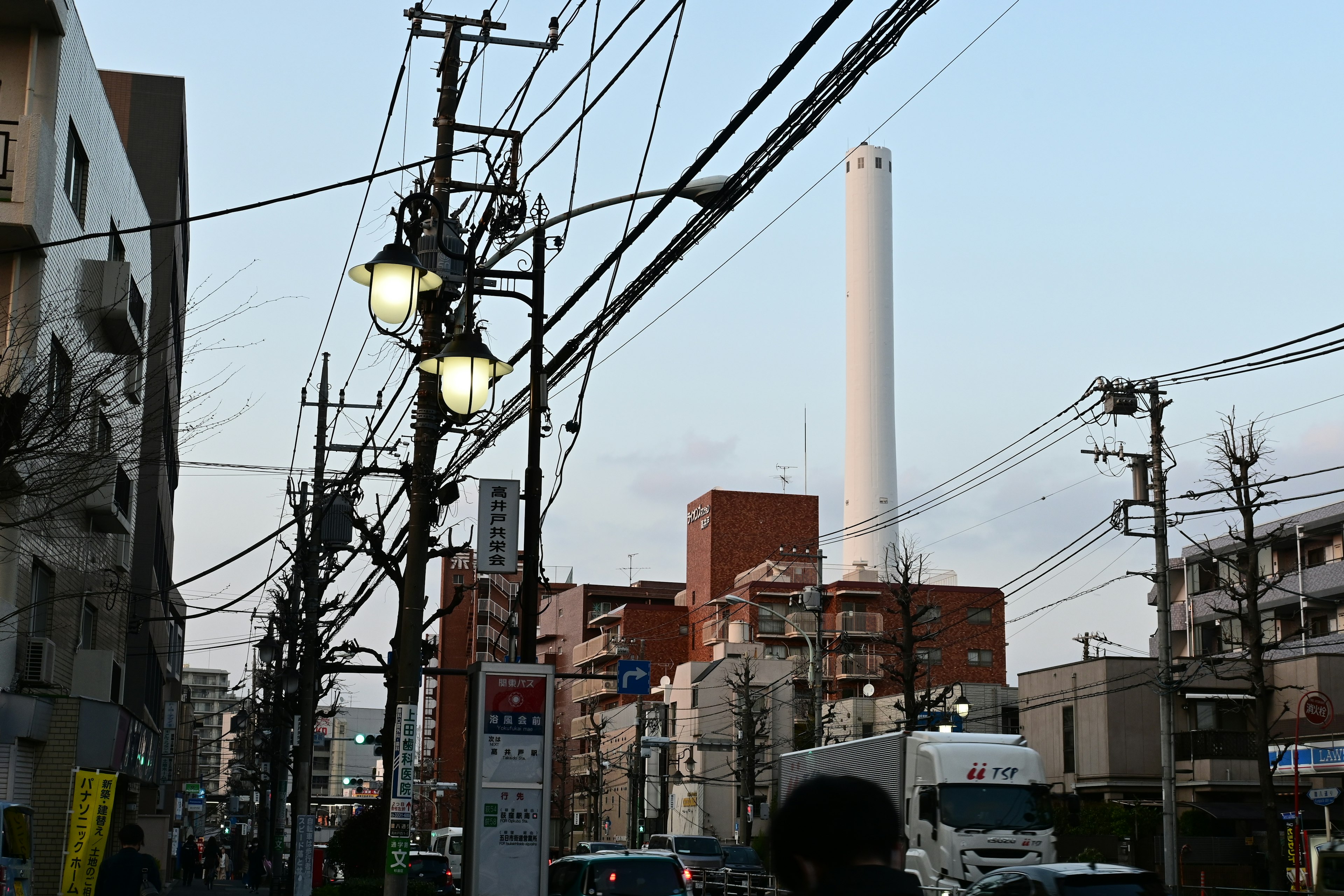 Paesaggio urbano al crepuscolo con linee elettriche e lampioni una alta ciminiera di fabbrica sullo sfondo