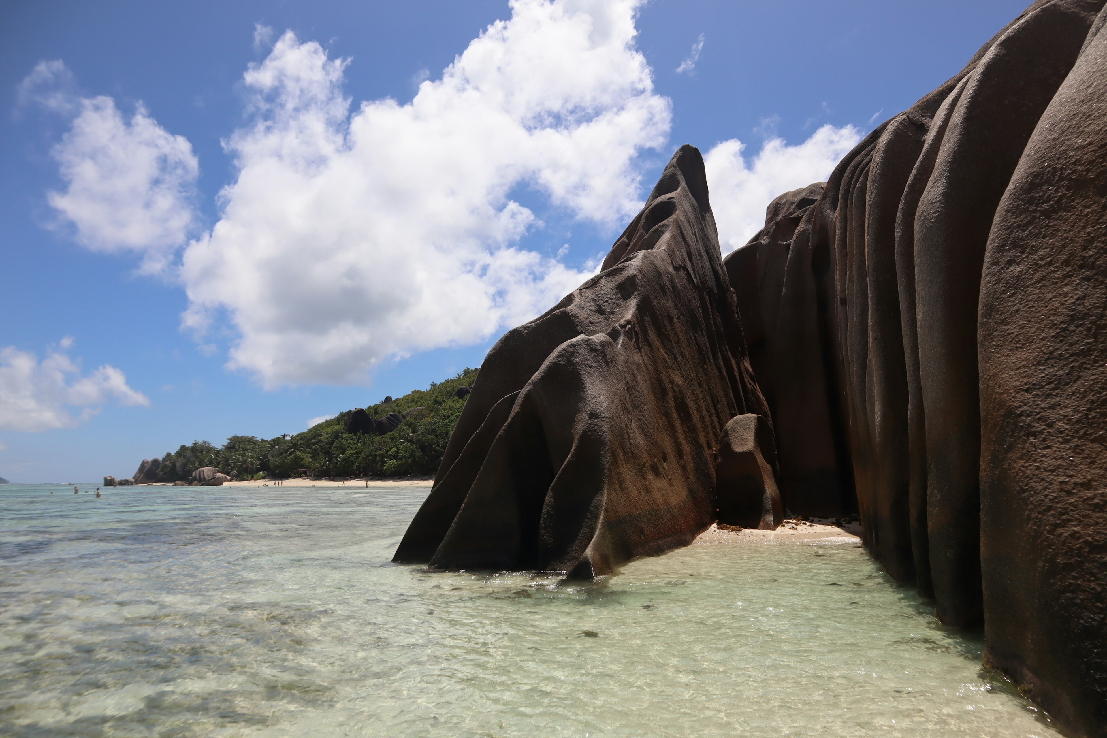 Large rock formations under a blue sky with clouds and clear water