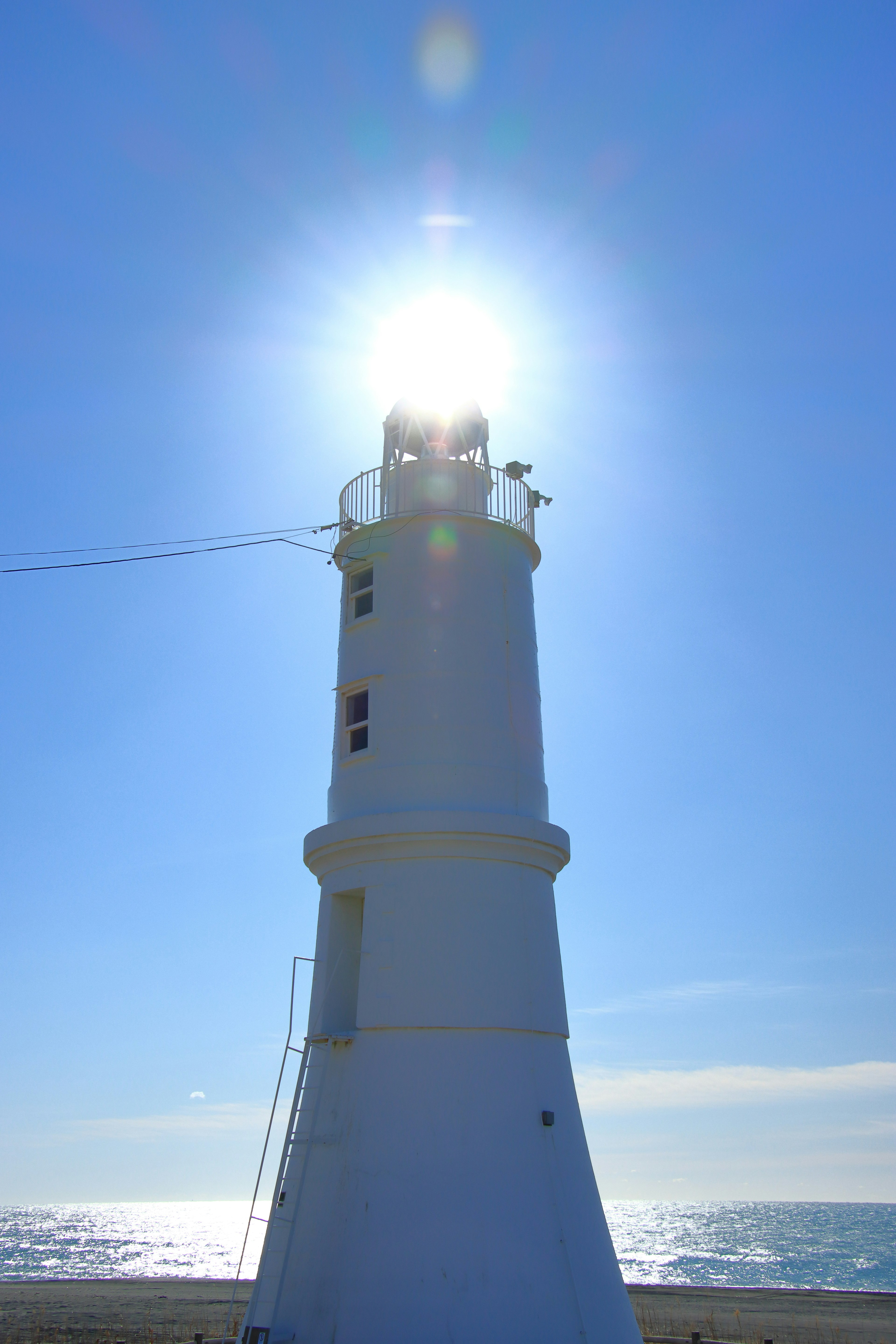 Faro bianco sotto un cielo blu chiaro con la luce del sole che brilla dalla cima