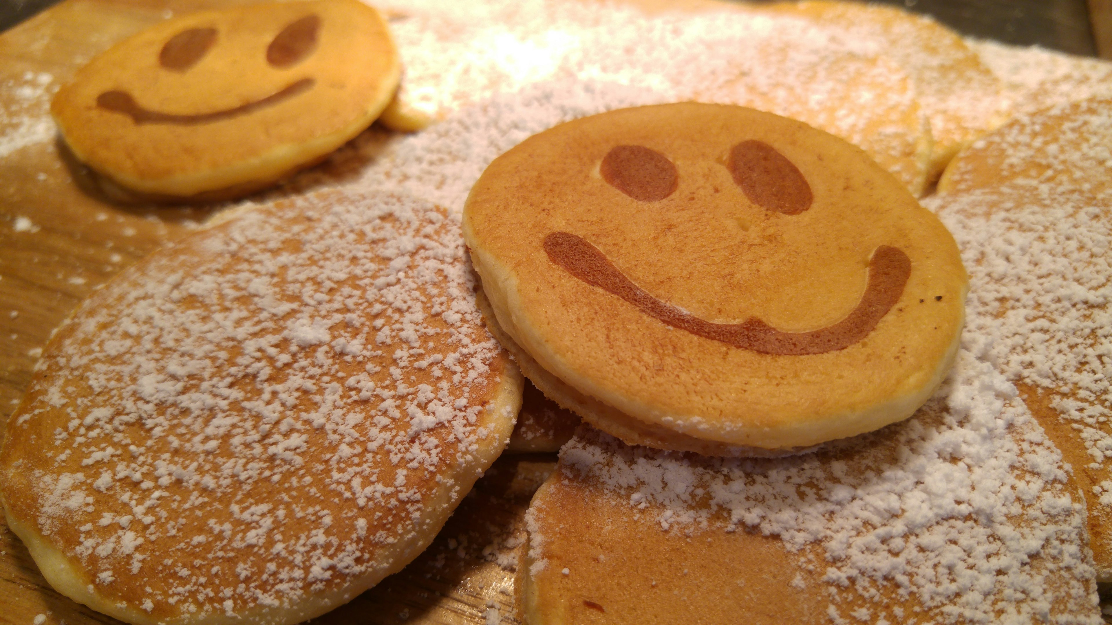 Sekumpulan pancake dengan desain wajah tersenyum dan gula bubuk yang ditaburkan di atasnya