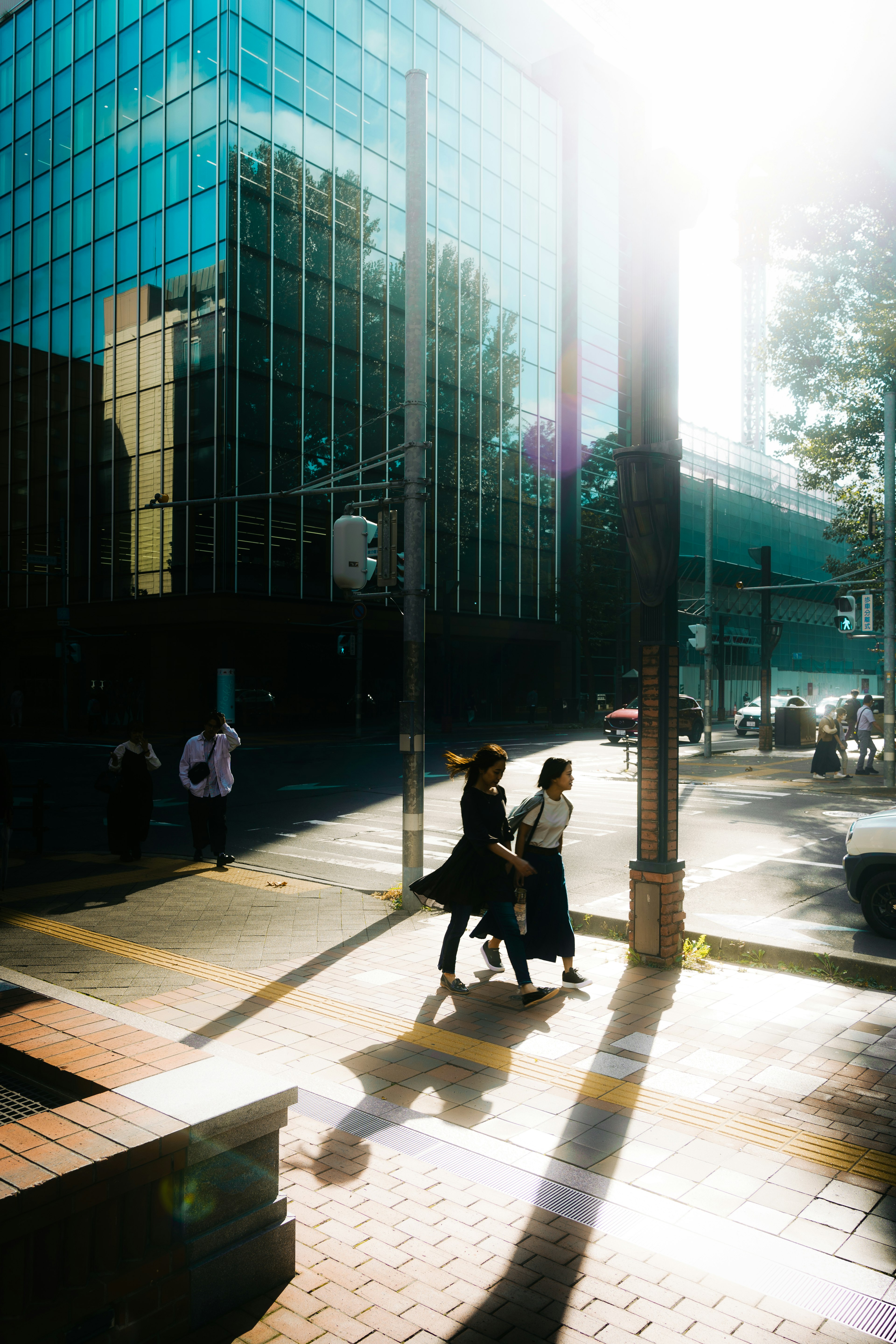 Dos personas caminando en una intersección urbana con reflejos de rascacielos