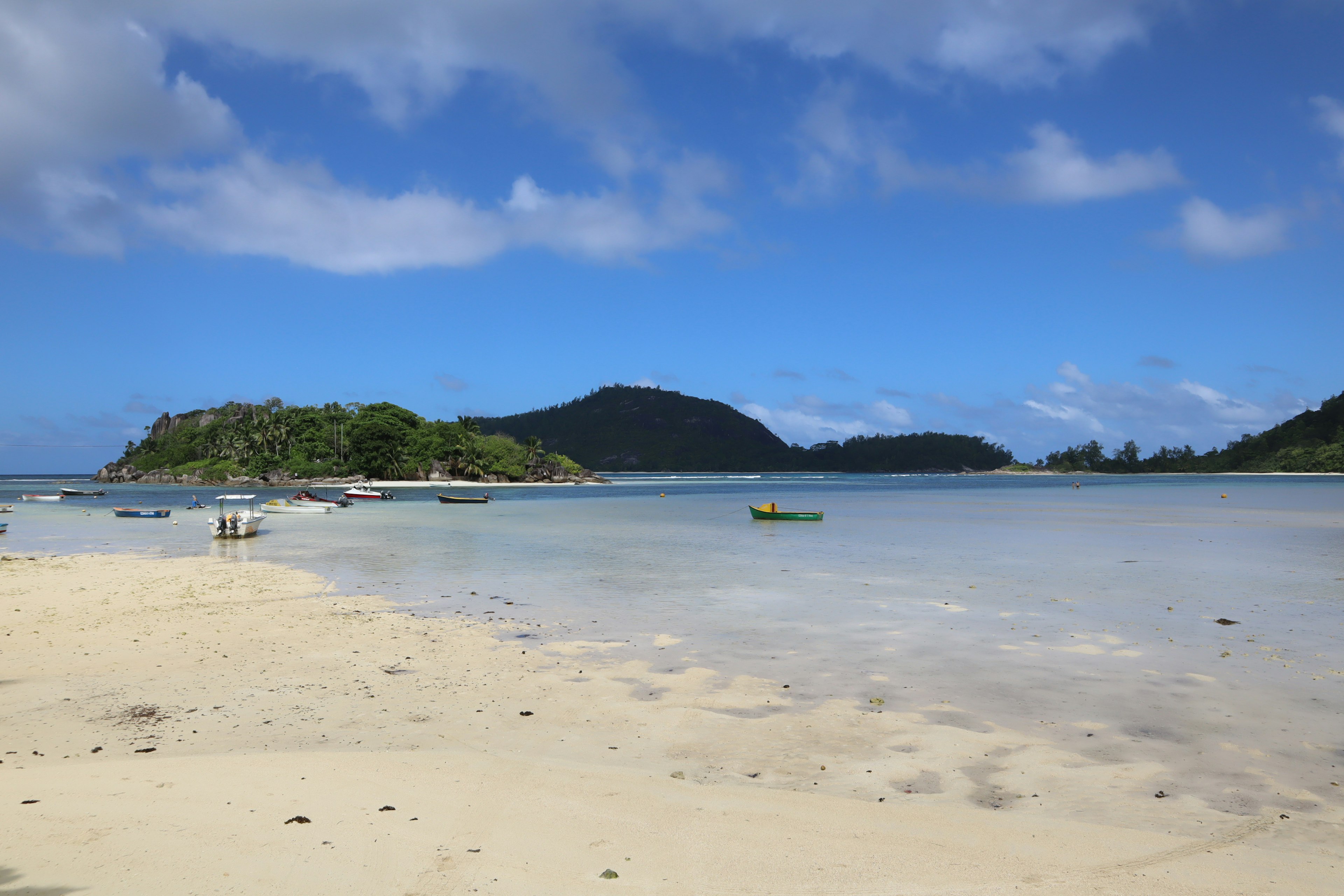 ทิวทัศน์ชายหาดที่สวยงามพร้อมท้องฟ้าสีฟ้าและทรายขาวมีเกาะสีเขียวและน้ำที่สงบ