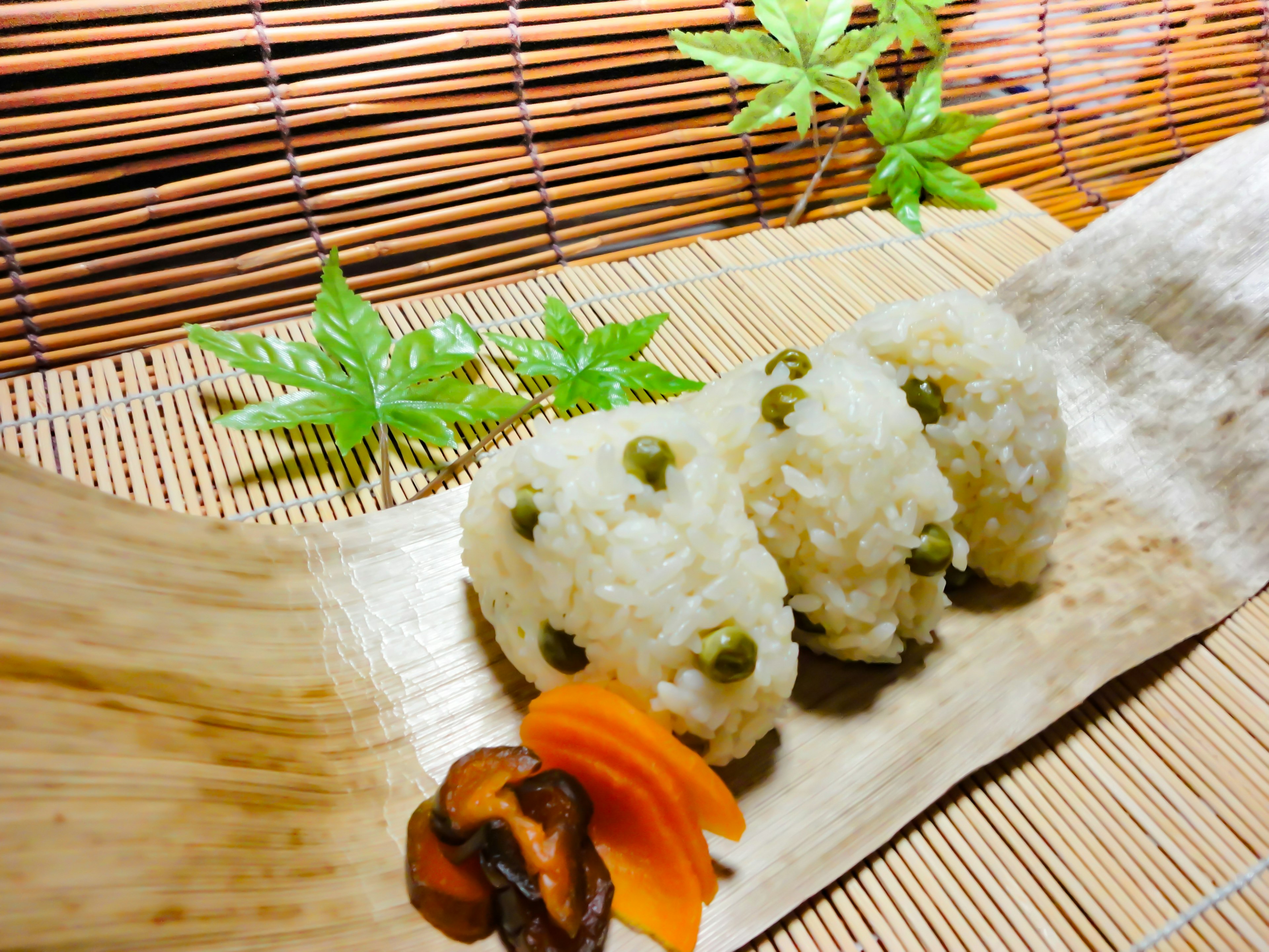 Tres deliciosas bolas de arroz dispuestas sobre hojas de bambú con verduras coloridas