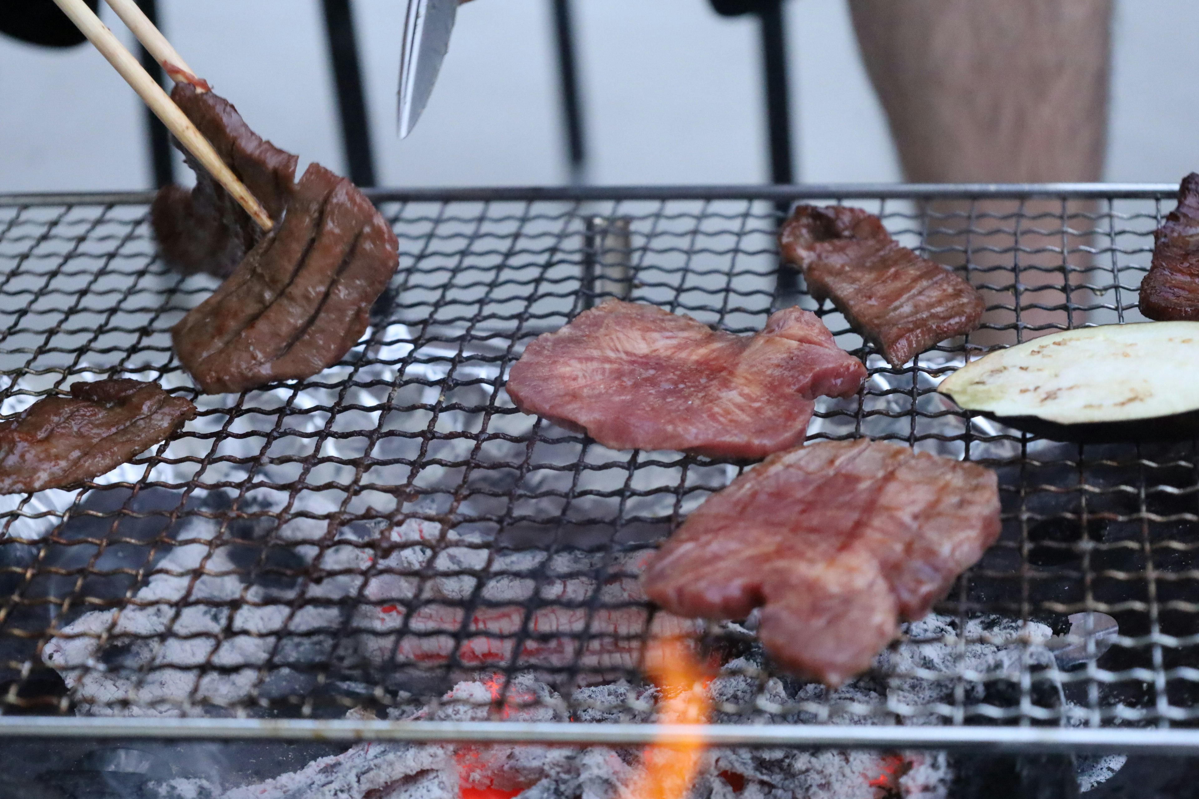 グリルで焼かれている肉のスライスと箸を持つ手