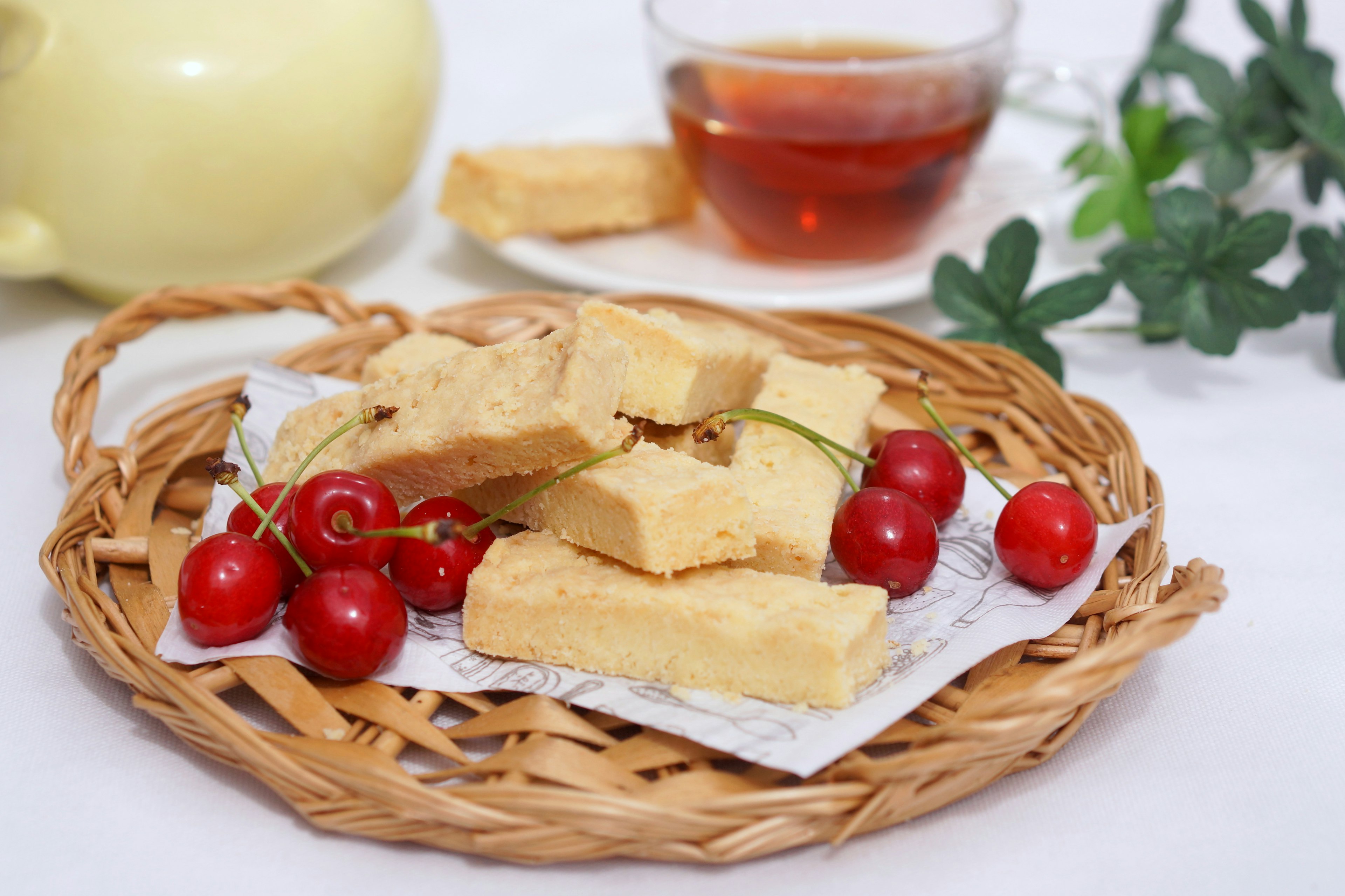 A basket with sweet treats and cherries alongside a cup of tea and teapot