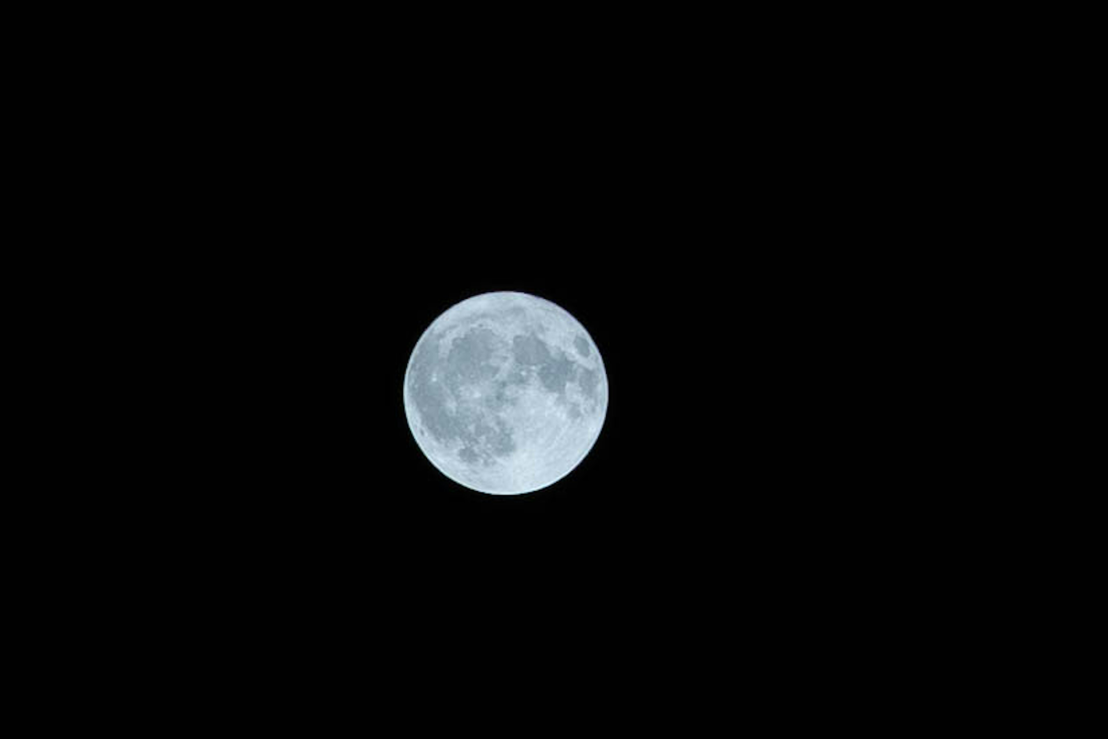 A pale blue moon glowing in the dark sky