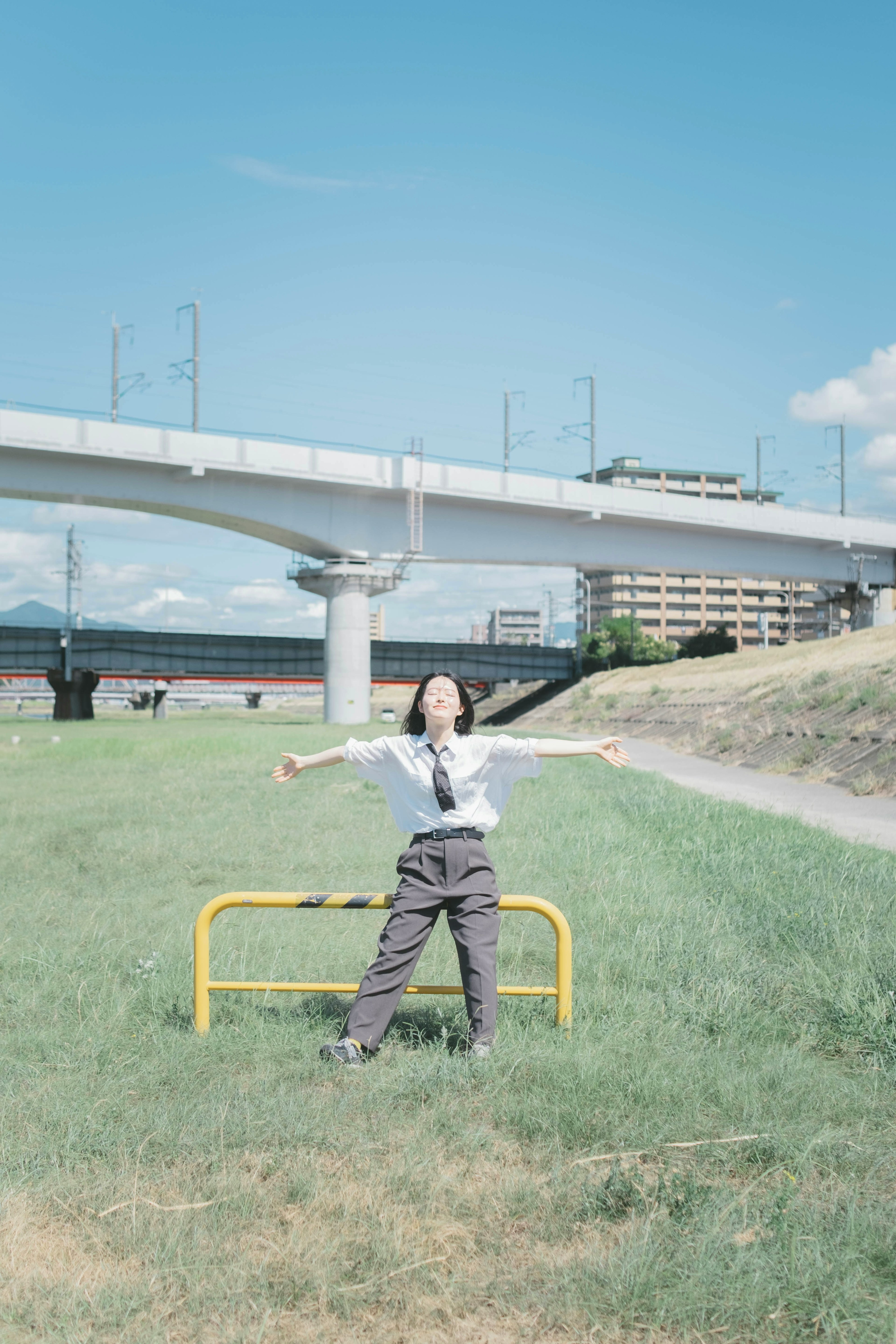 青空の下で両手を広げている女性が黄色のバリケードの前に立っている風景